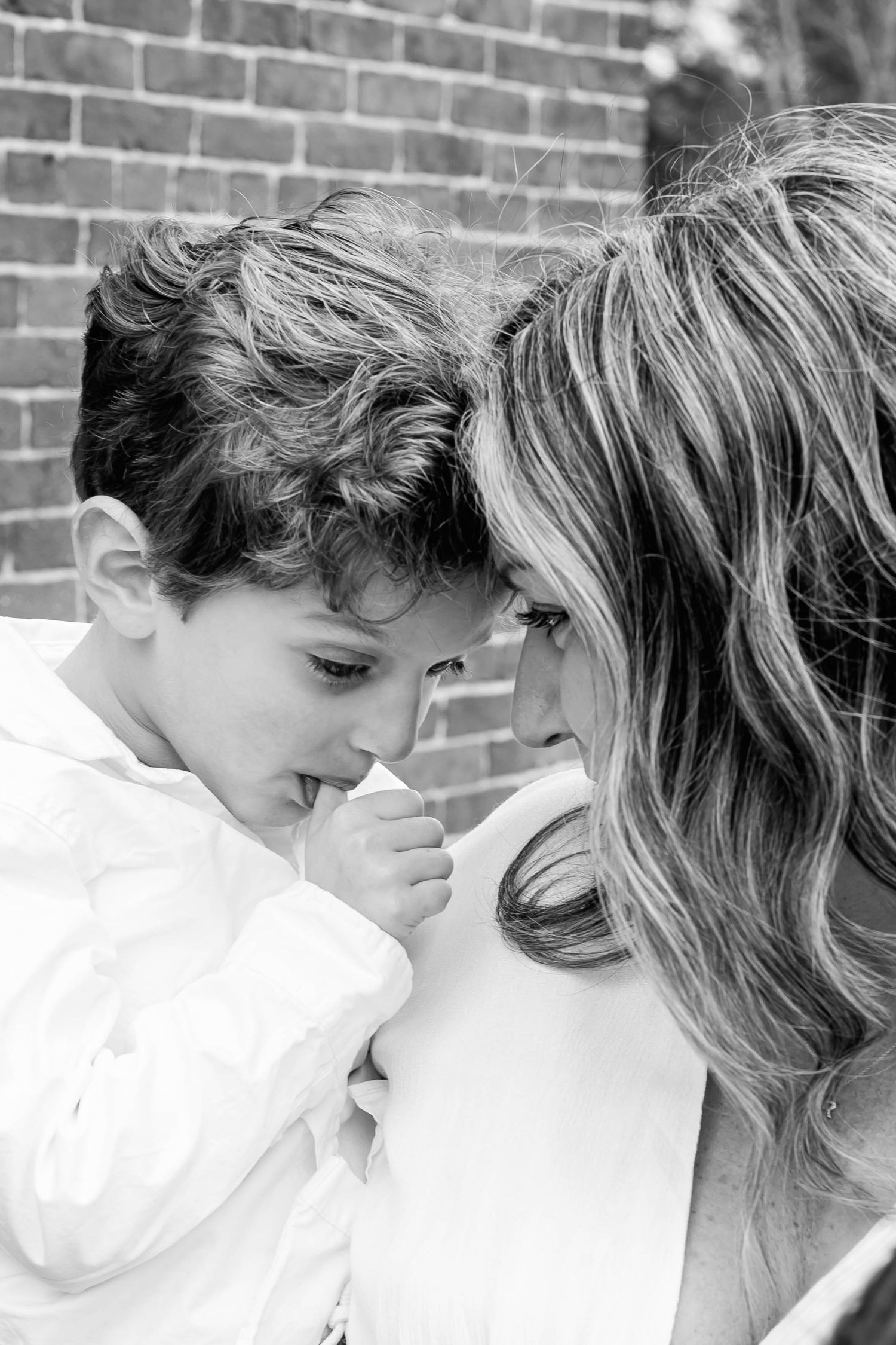 Black and white close-up capturing an intimate moment between parent and child against a brick wall.