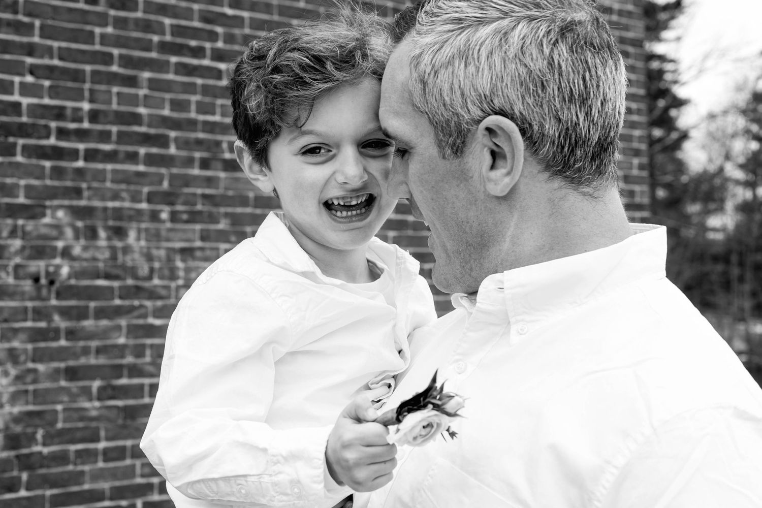 Black and white portrait of shared laughter between parent and child against brick wall.