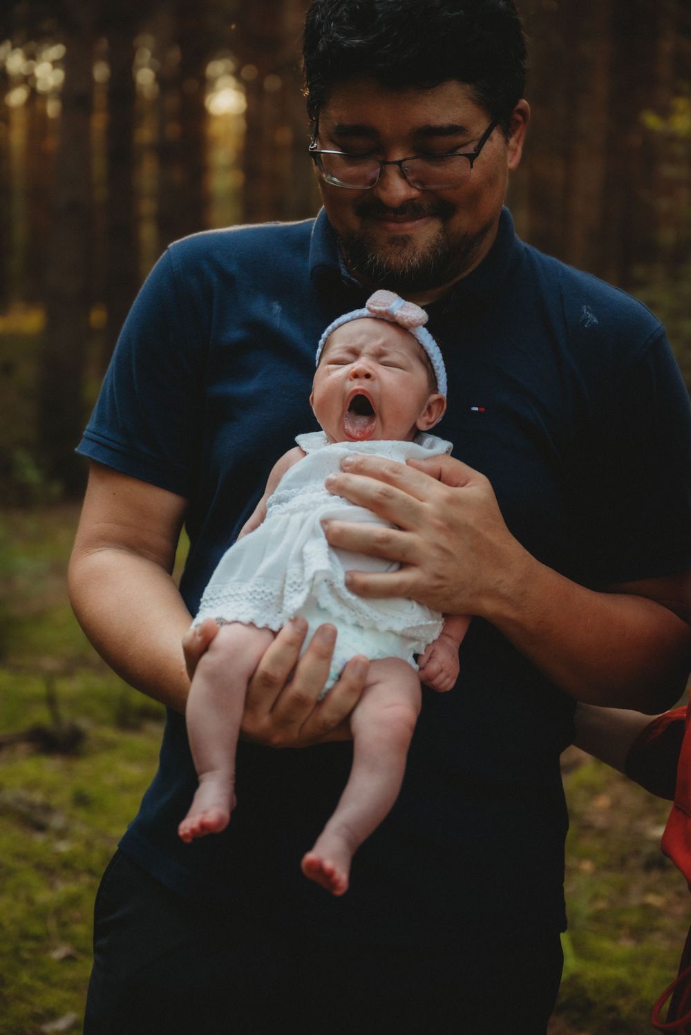 A happy moment as a baby yawns while being held in a forest setting.