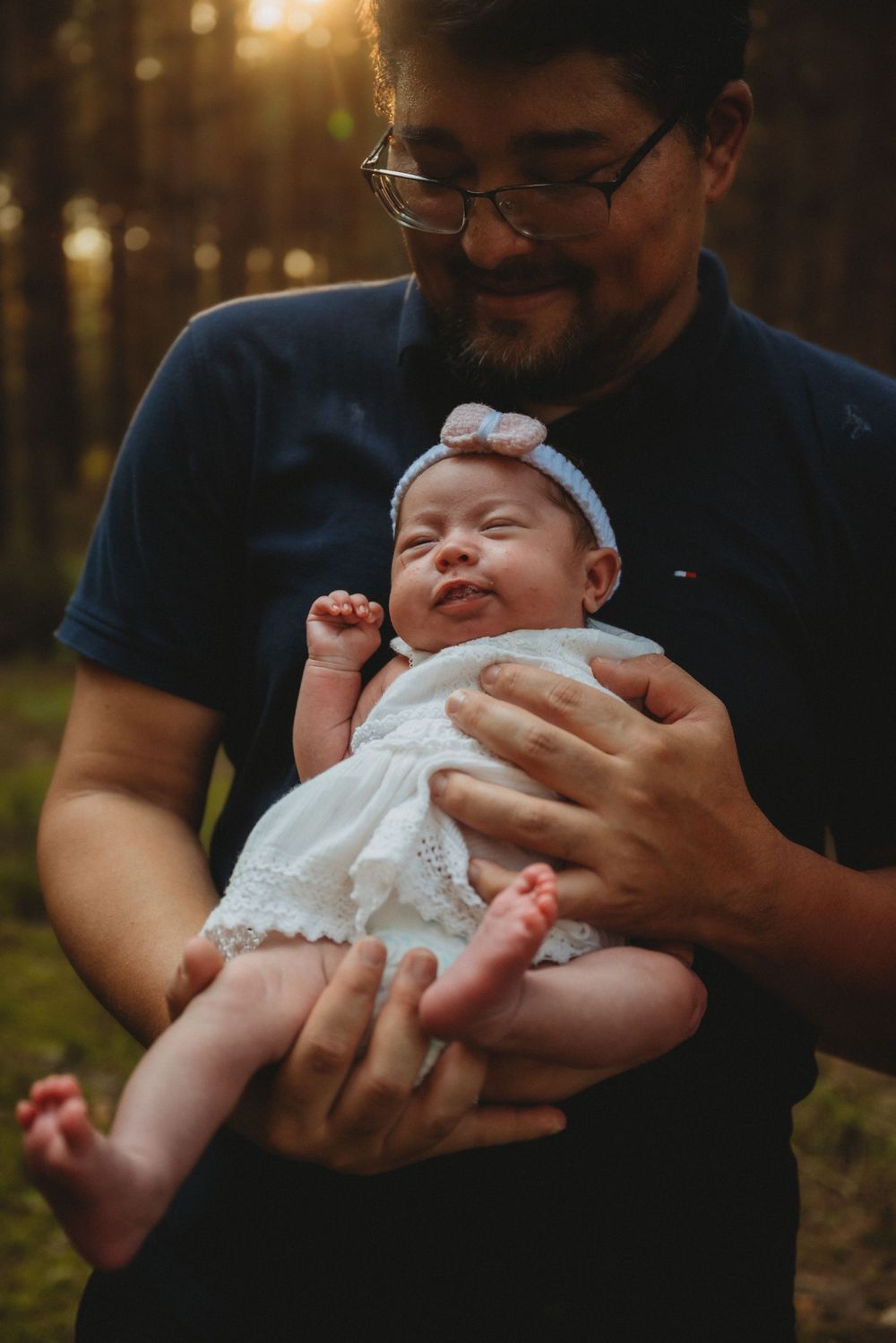A delightful moment as a smiling baby stretches while being held in dappled forest light.