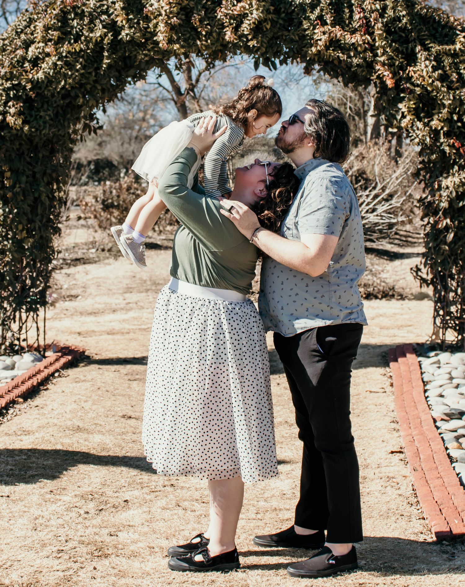 A joyful family moment captured under a floral arch in a garden setting.