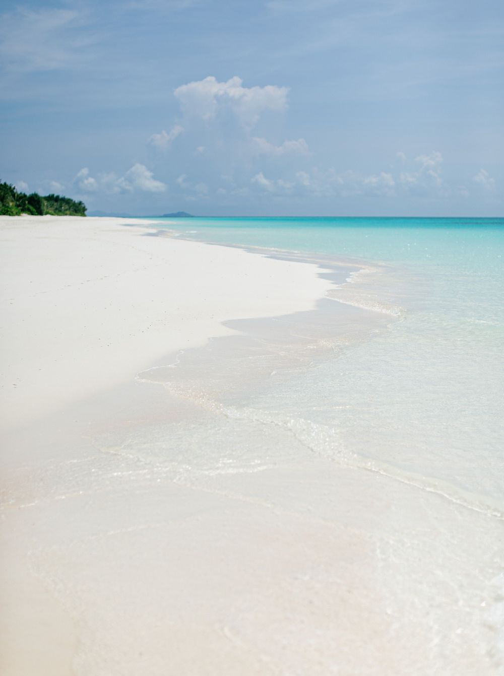 A serene beach at Amanpulo, Philippines: white sand, crystal-clear water, and a picturesque blue sky.
