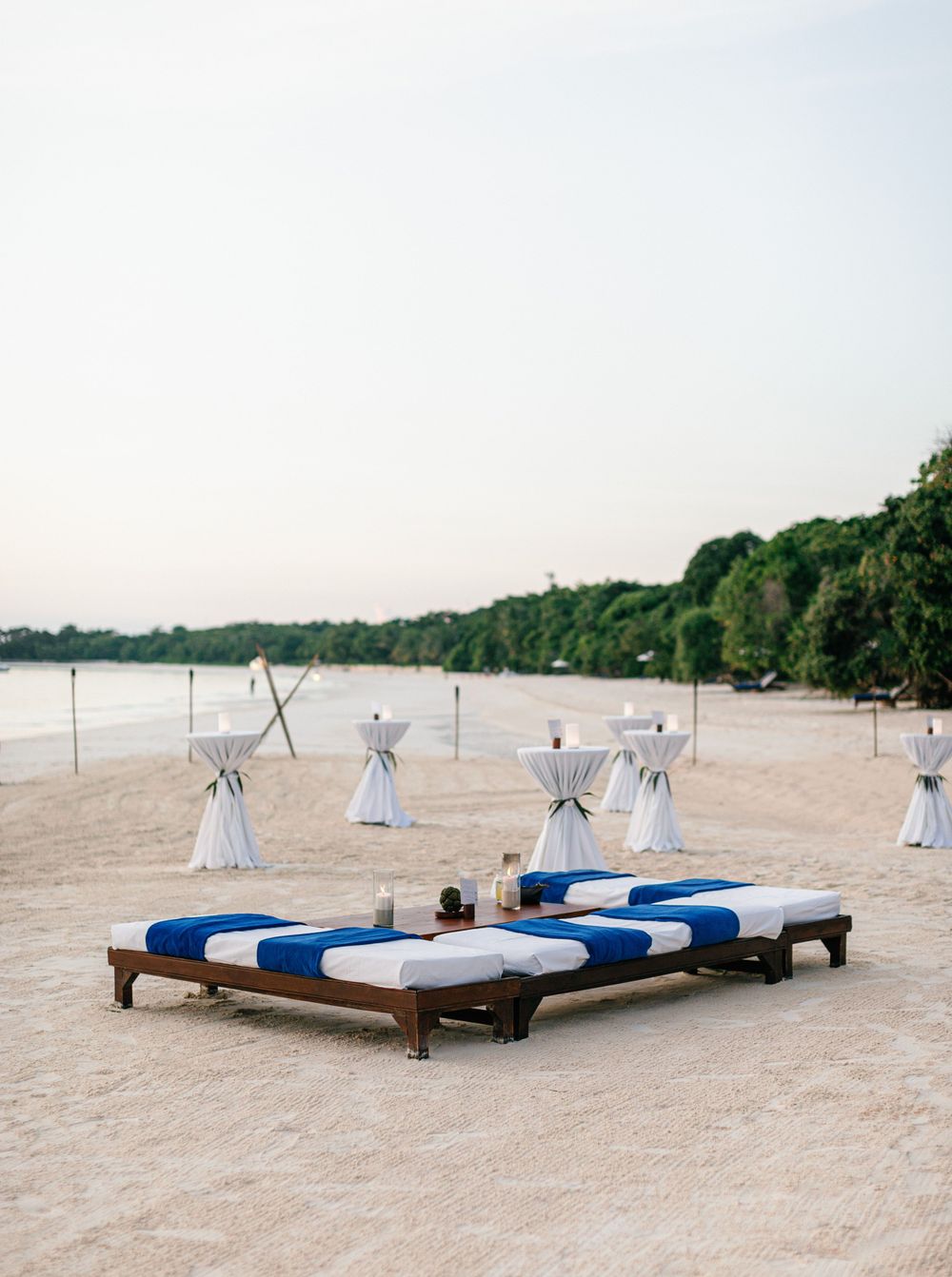 A serene beach at Amanpulo, Philippines, adorned with blue and white pillows and tables for a relaxing cocktail setting