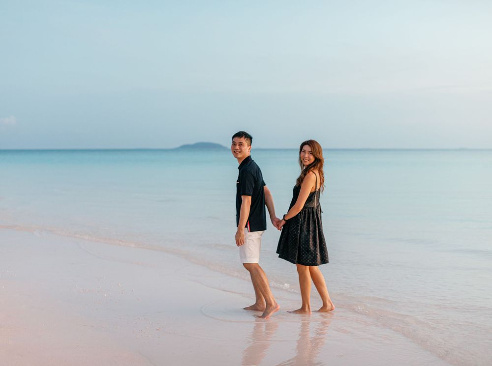 A bride and groom on the beach at Amanpulo, Philippines, standing together and holding hands.