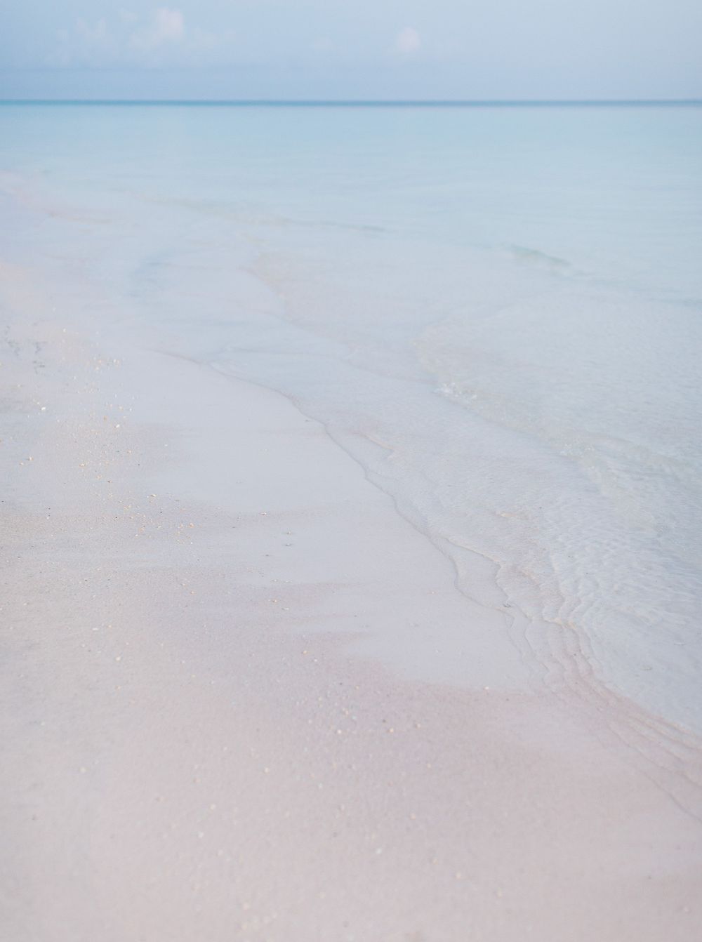 A tranquil beach at Amanpulo, Philippines: white sand, clear water, and a blue sky.