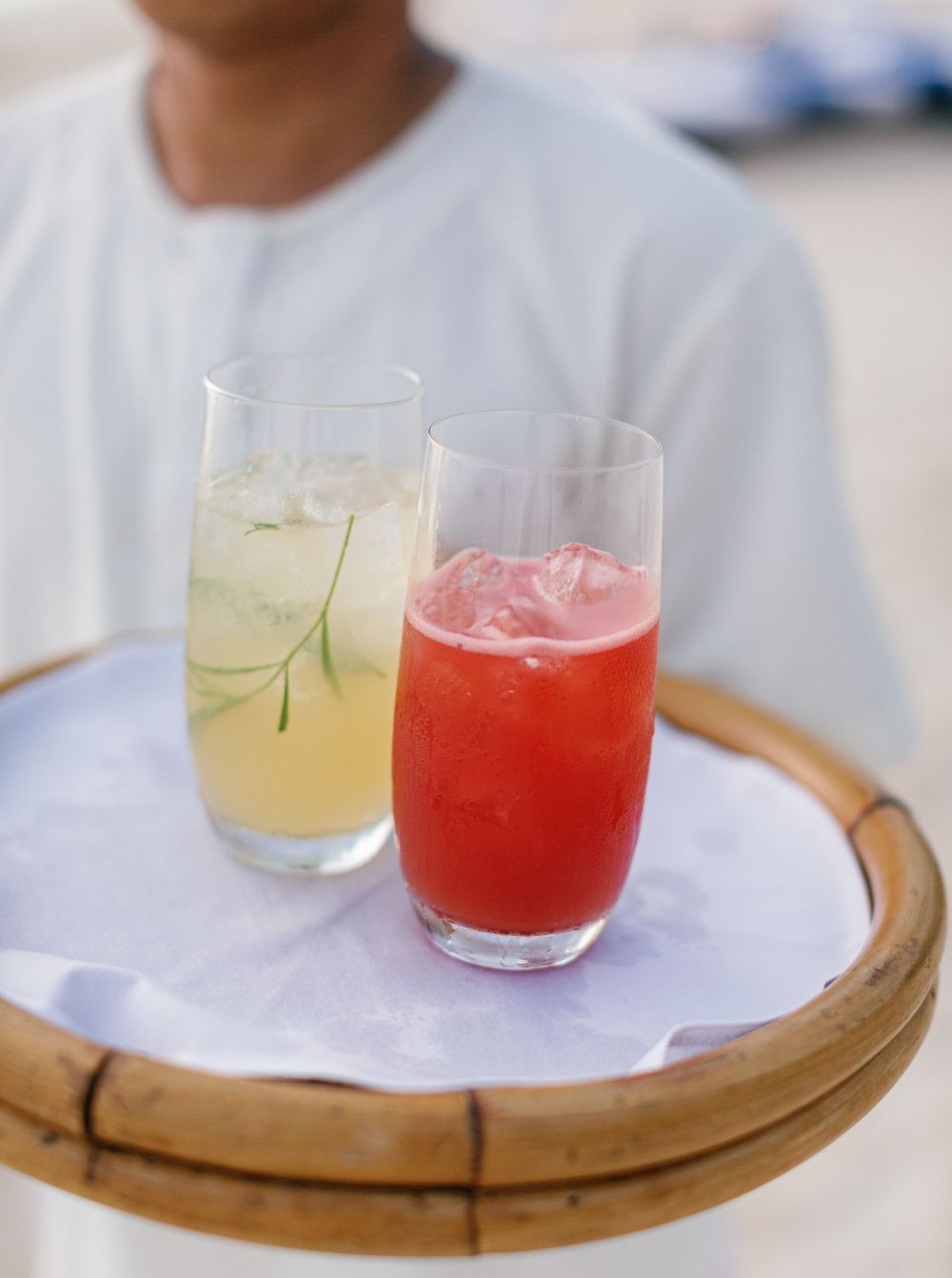 A man holding a tray with two drinks on it, serving a cocktail on the beach at Amanpulo, Philippines.