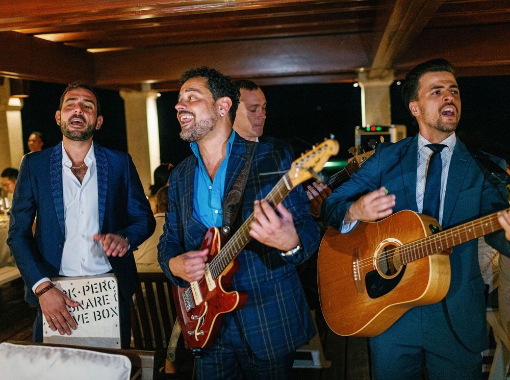A group of men in suits playing guitar at a wedding celebration in Amanpulo, Philippines.