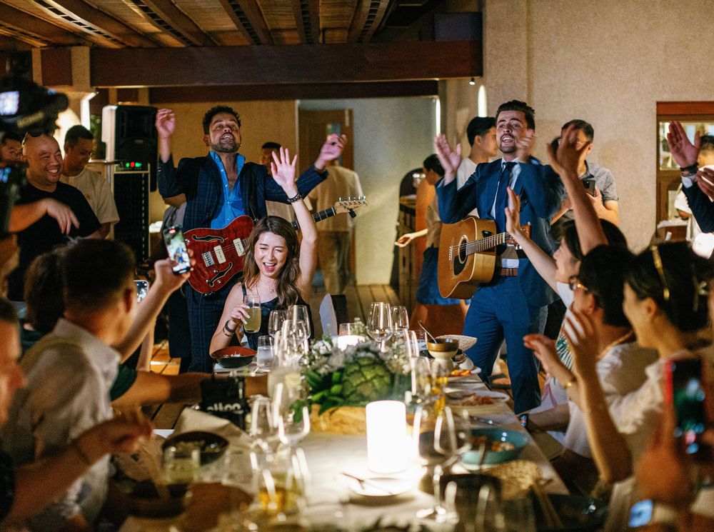 Wedding guests cheering with hands up, musicians playing at Amanpulo, Philippines celebration.