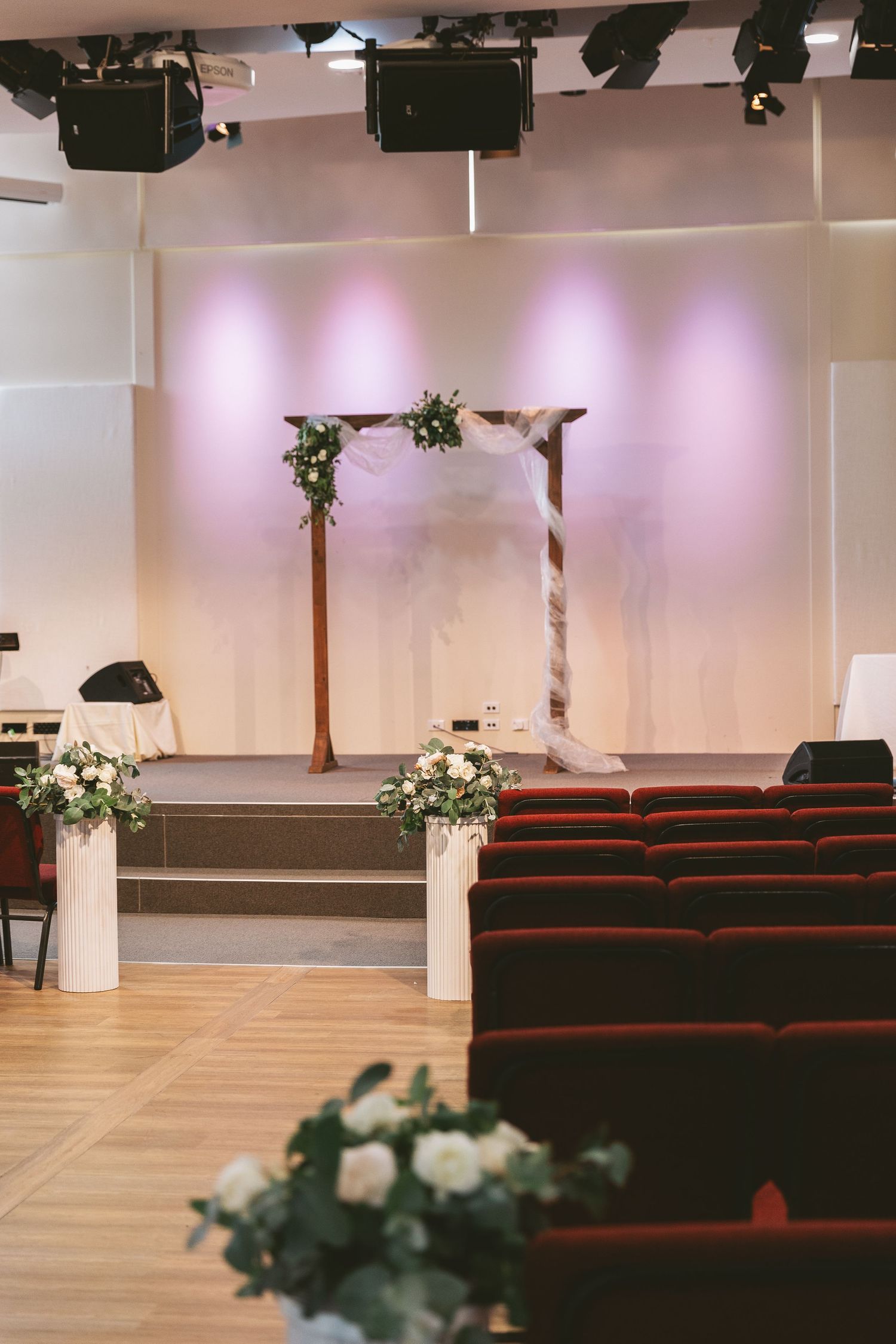 Wedding ceremony venue with wooden arch decorated with white flowers and red theater seating.