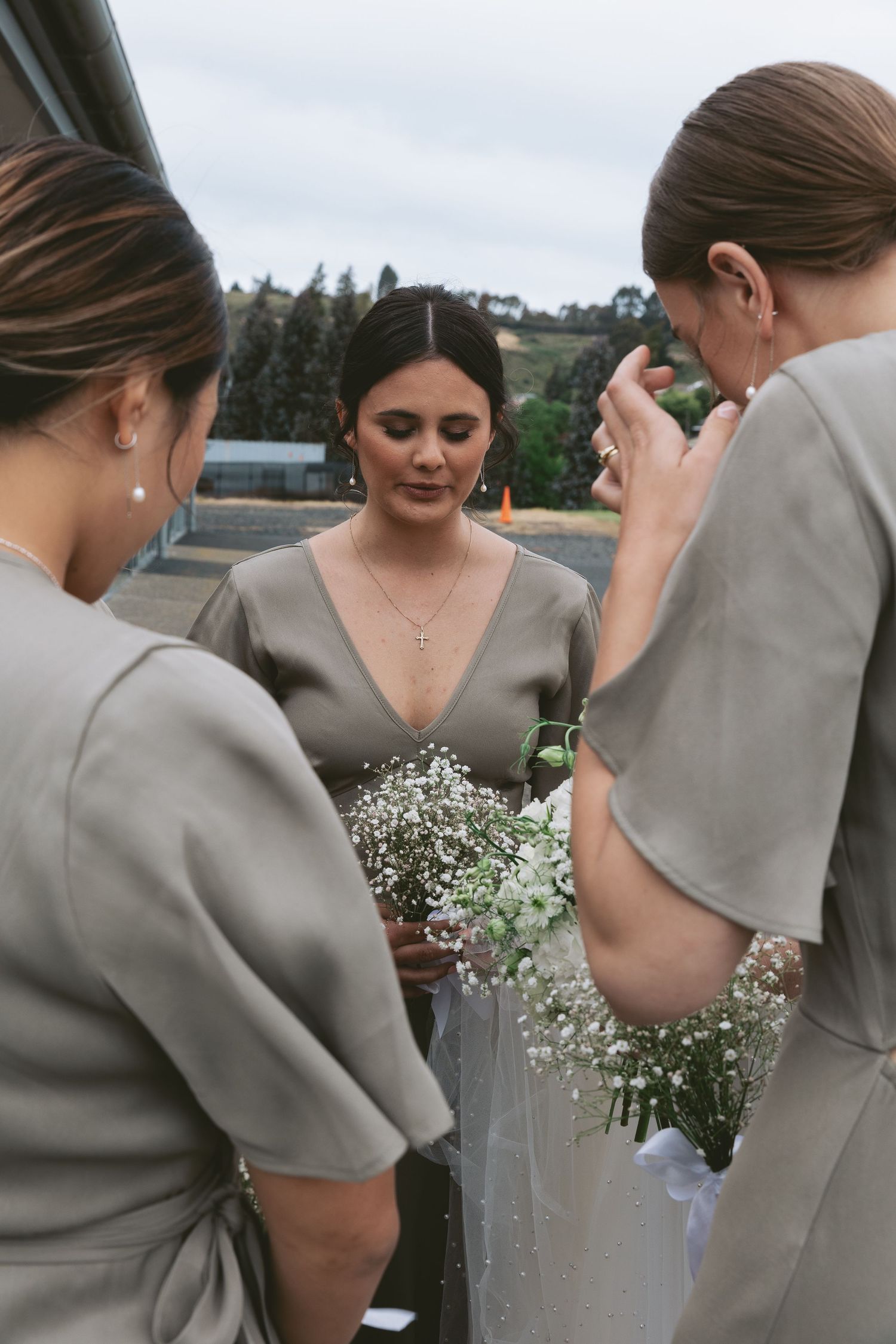 Wedding party in sage colored dresses gathered together holding delicate white floral bouquets.