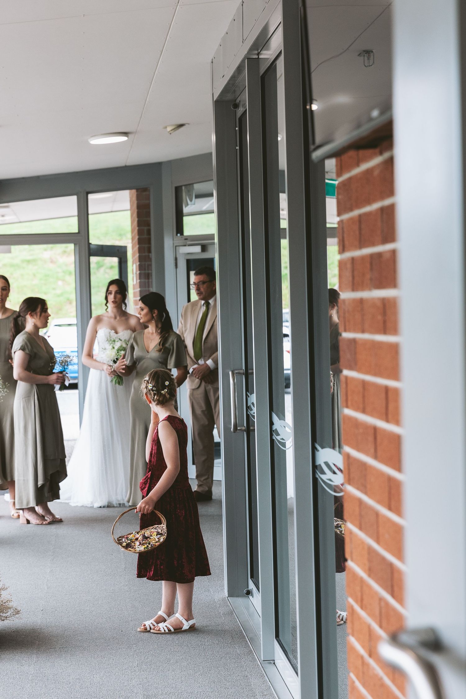 Wedding party gathers in a modern corridor with brick and glass walls.