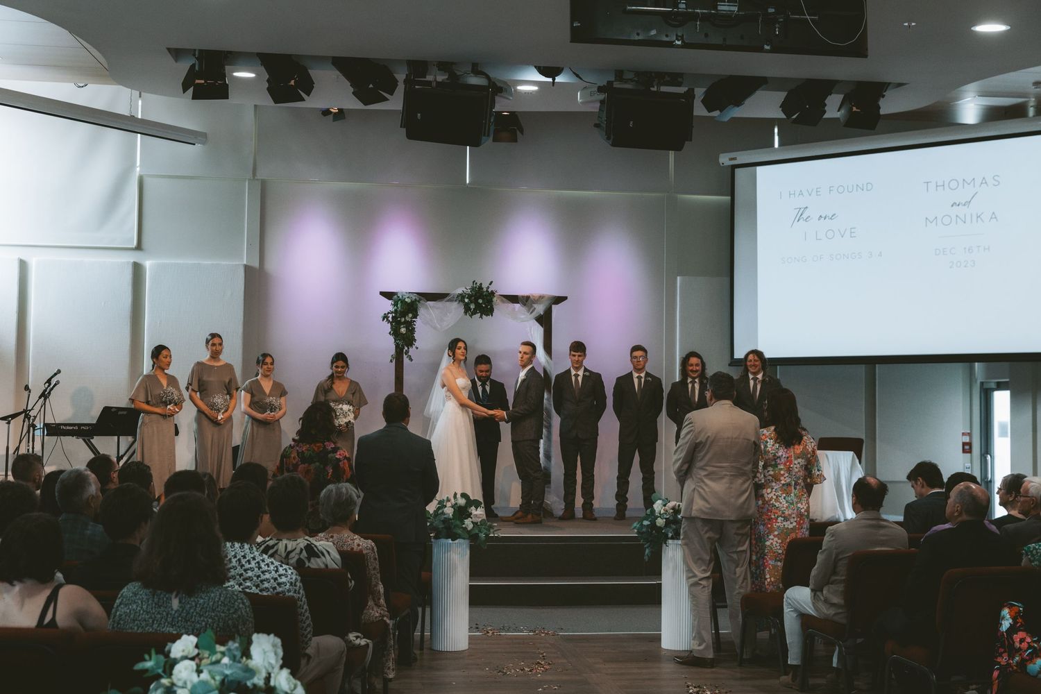 Wedding ceremony in progress on stage with purple lighting and cross backdrop.
