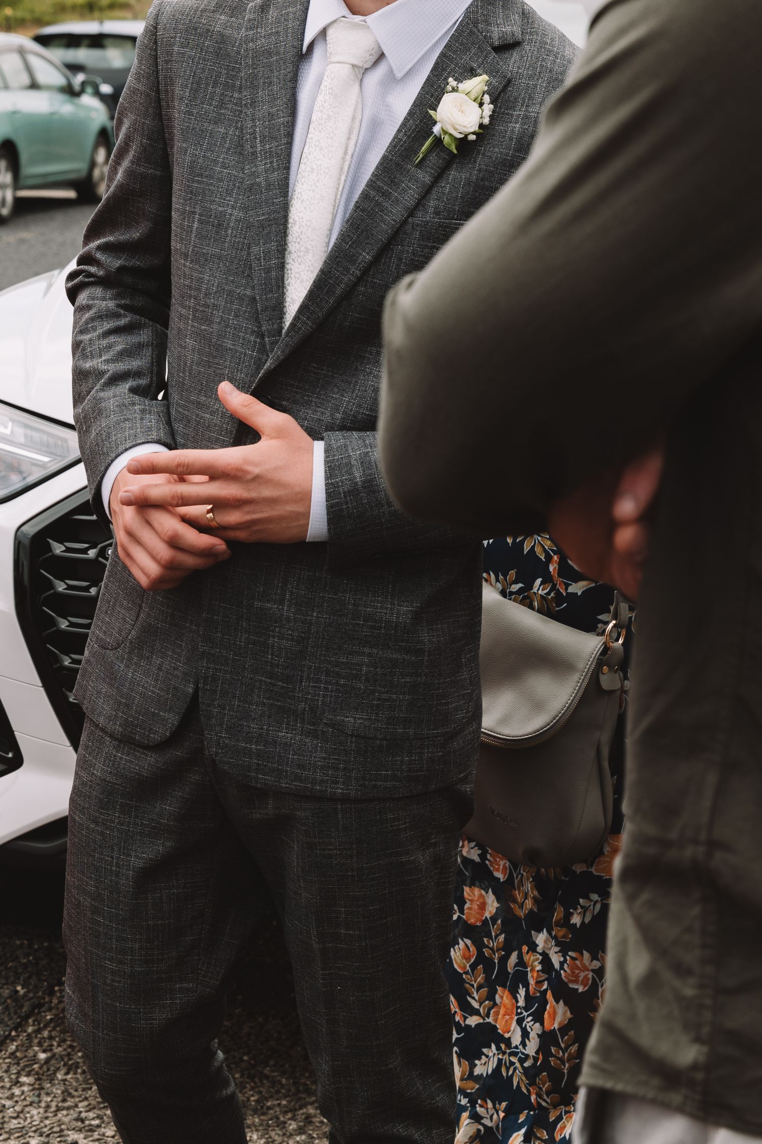 A groom in a gray suit with white boutonniere clasps hands during a wedding moment.