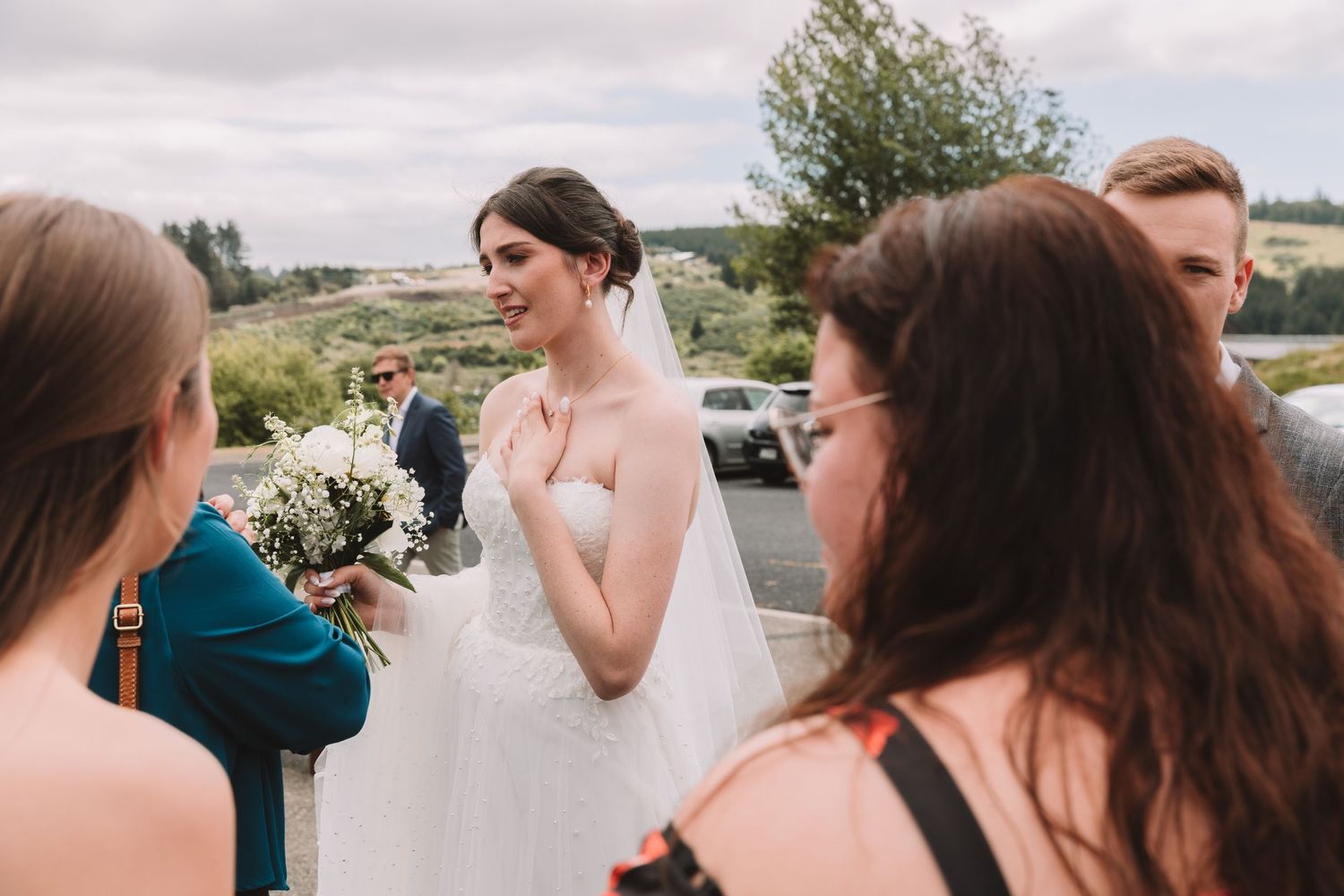 A white wedding gown and simple bouquet are captured during an outdoor gathering.