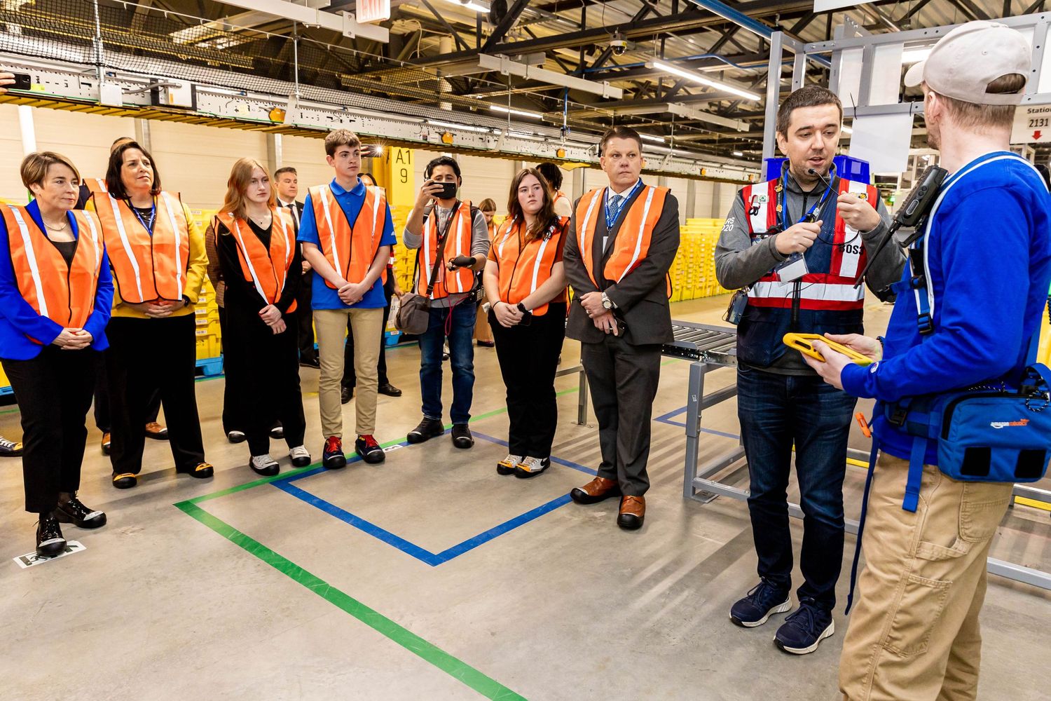 Warehouse tour group wearing safety vests listening to a presentation in an industrial facility.