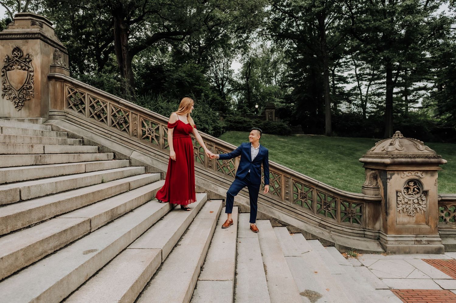 A couple in formal attire poses on elegant stone steps with ornate railings in an outdoor setting.