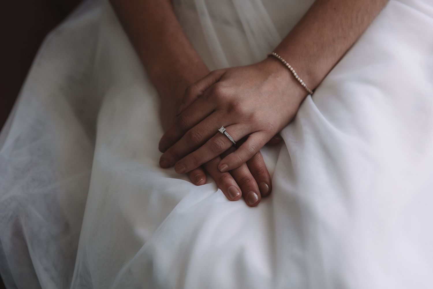 Close-up detail shot of hands with a wedding ring resting on white fabric.