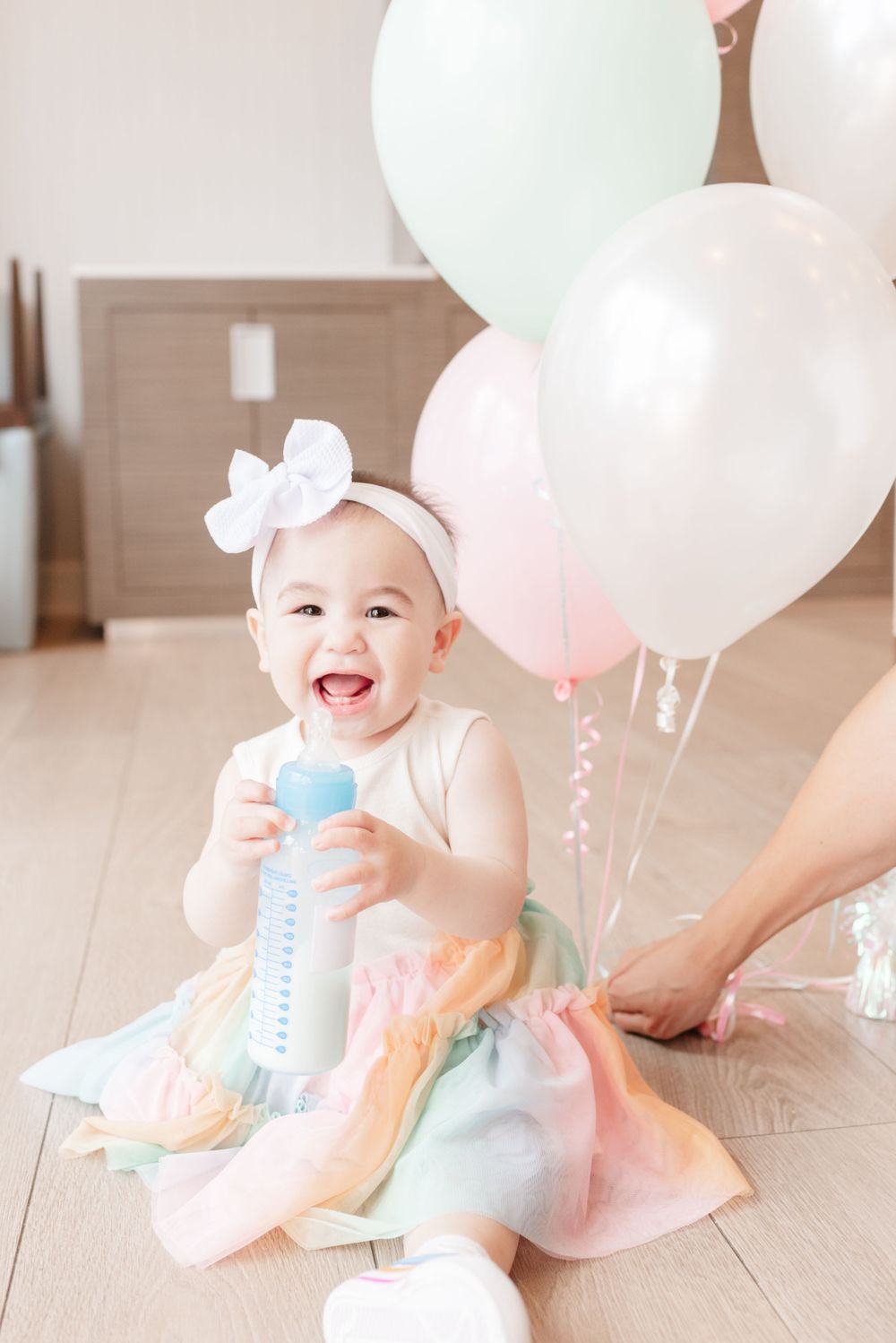 Toronto first Birthday girl smiling wearing birthday outfit standing by balloons, captured by Toronto photographer