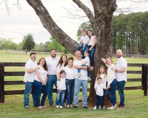 Large extended family wearing coordinating white and denim outfits poses together by rustic fence.