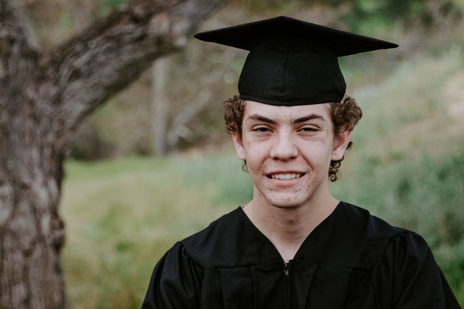 Graduate in black cap and gown smiling for an outdoor portrait.