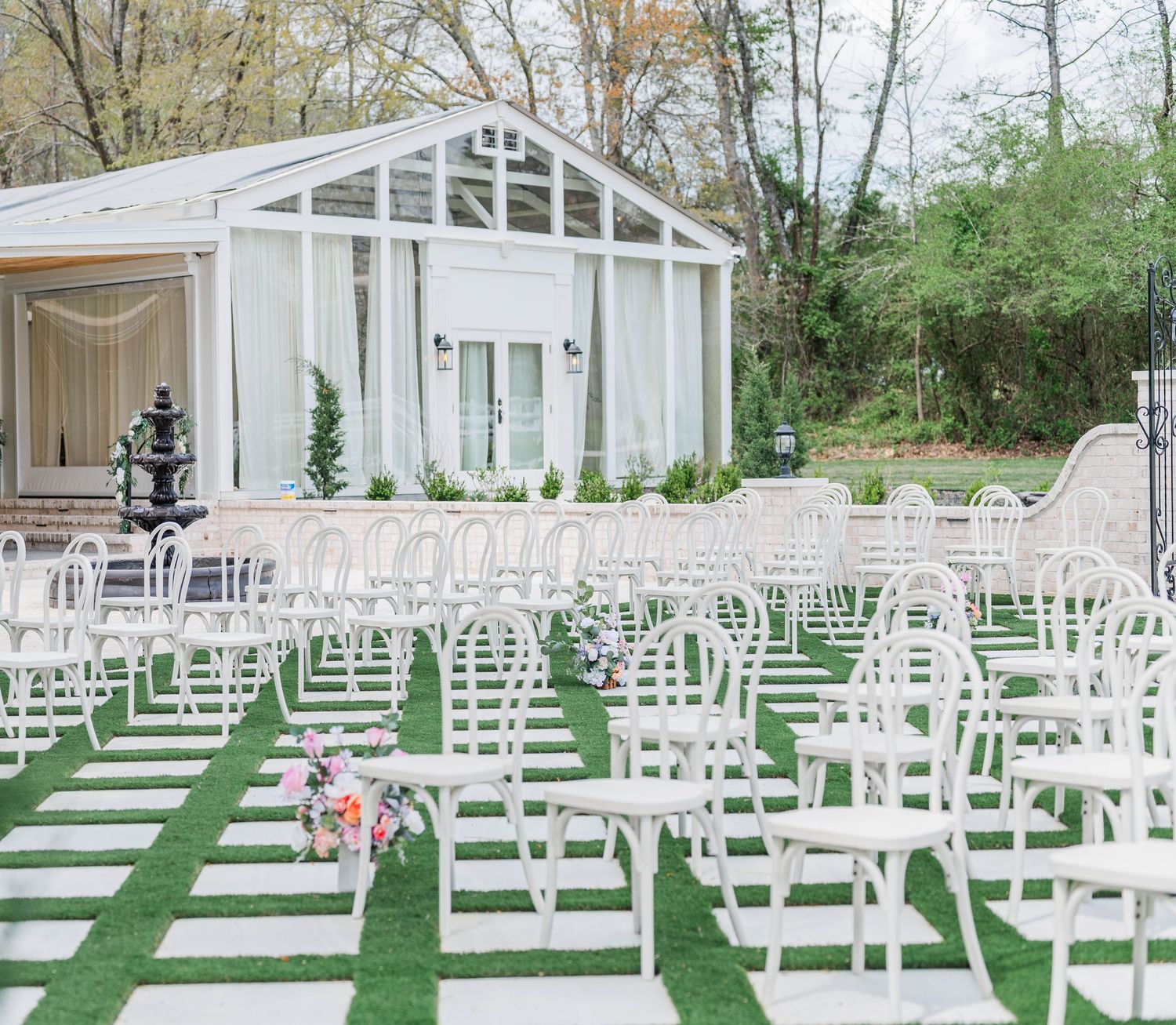 Elegant white wedding chapel with glass walls and rows of white chairs arranged on green grass for an outdoor ceremony.