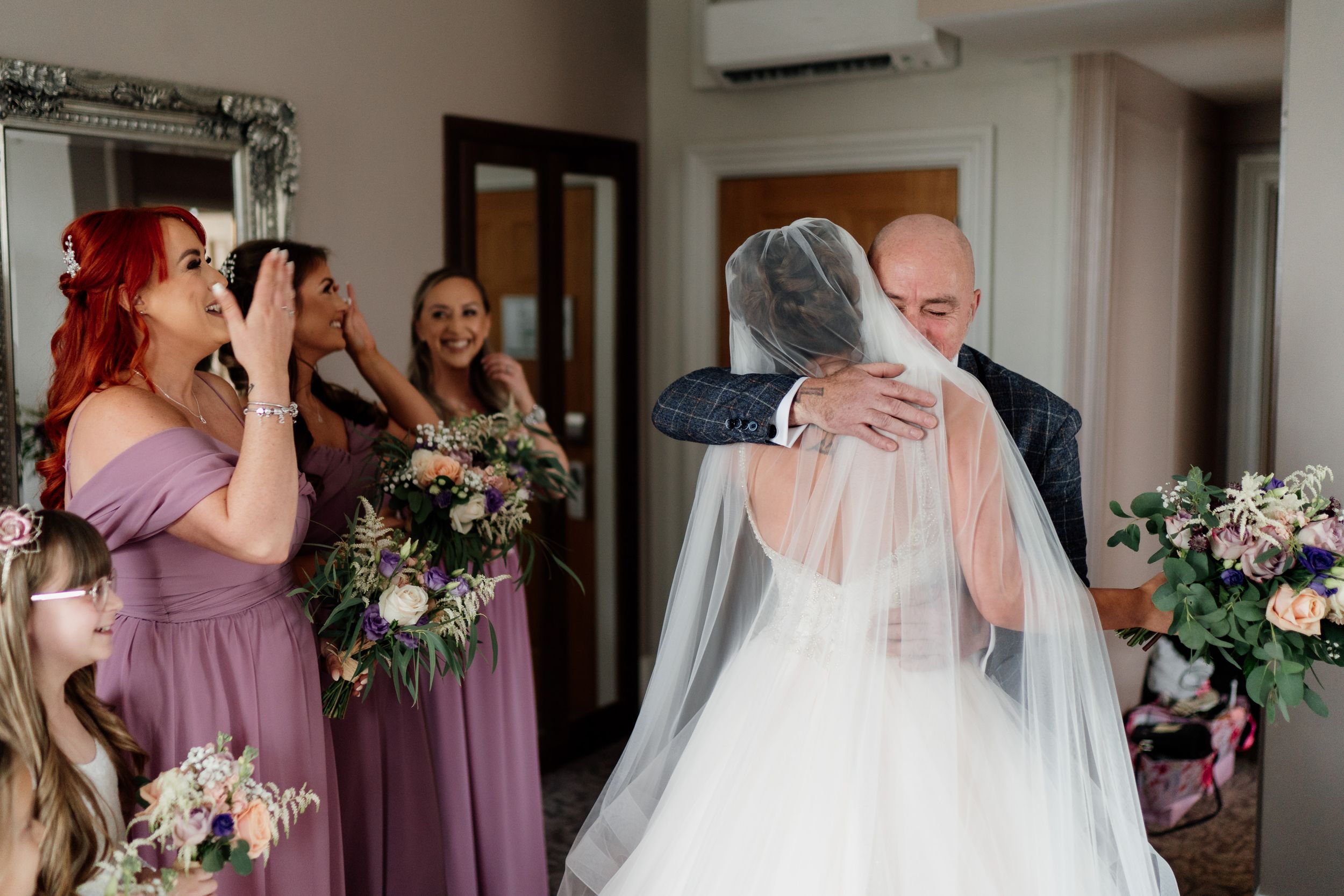 Emotional first look moment captured with bridesmaids in mauve dresses looking on.