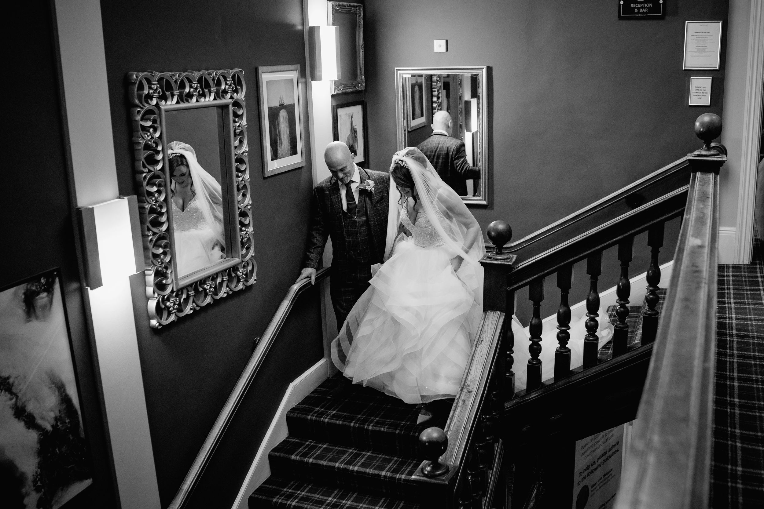 Black and white image of couple descending elegant staircase before wedding ceremony at Barton Hall.