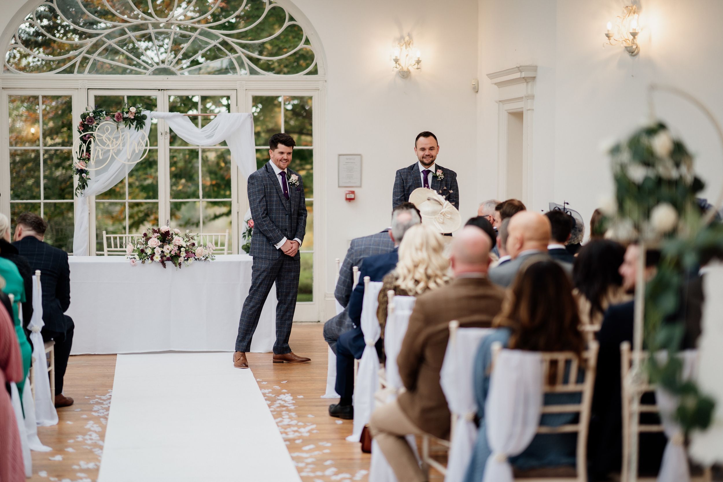 Wedding ceremony at Barton Hall in a bright venue with white chairs and arched windows.
