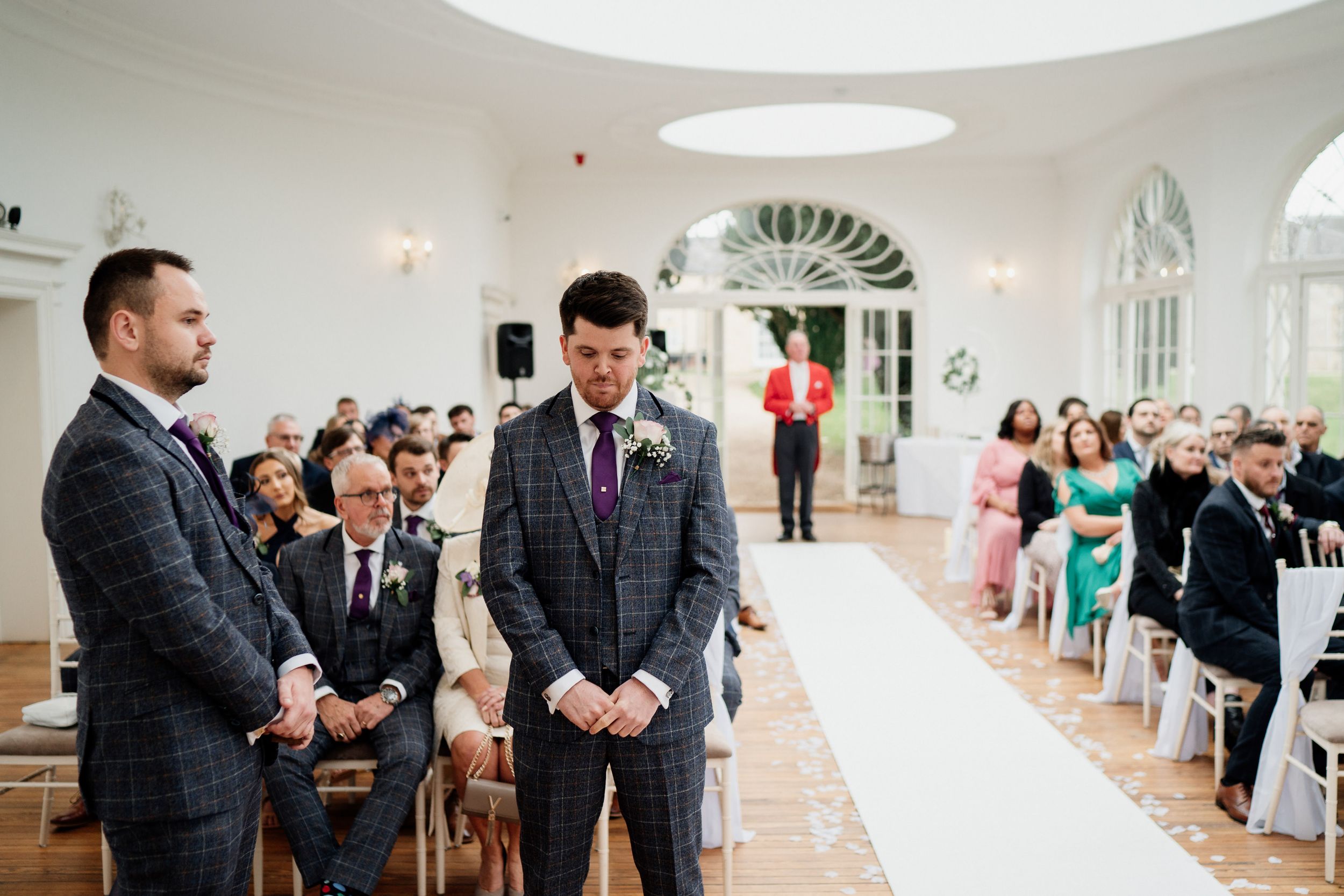 Wedding guests seated in white chairs watch as ceremony begins in elegant white room of Barton Hall.