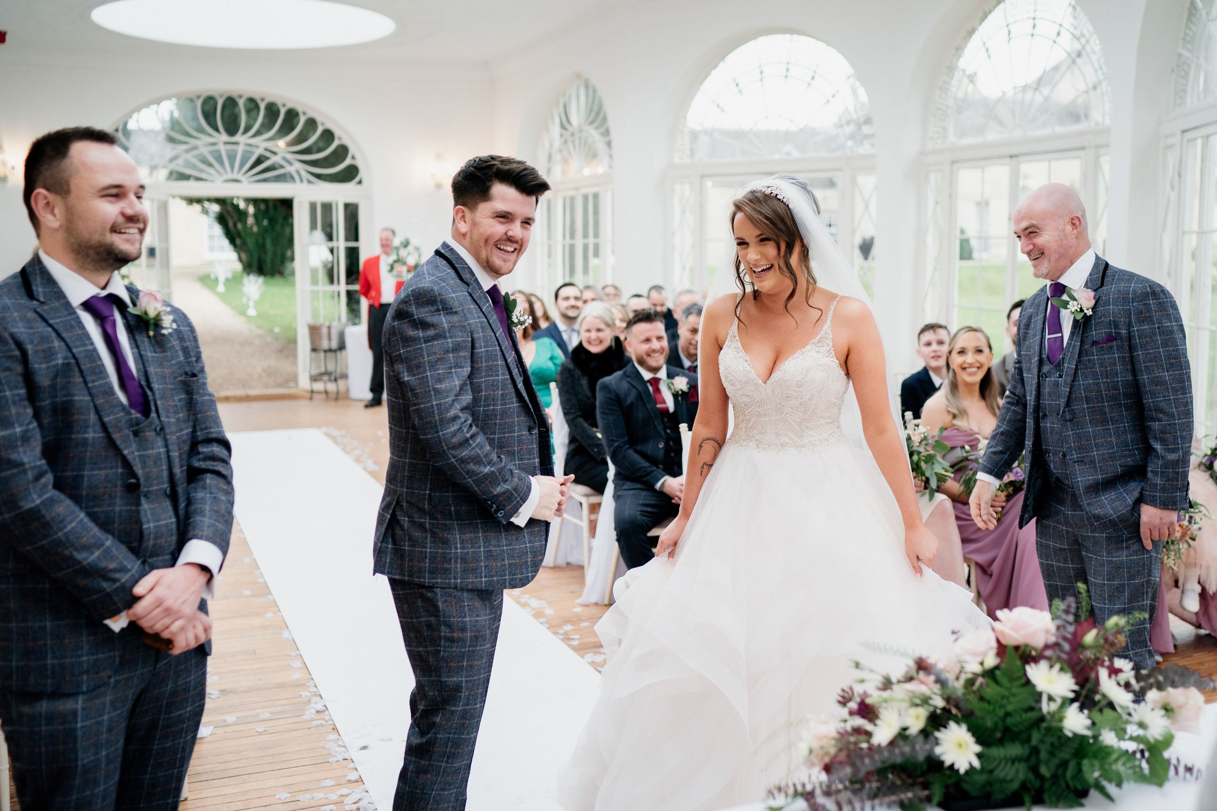 Wedding ceremony in bright indoor venue with elegant decor and white chairs.