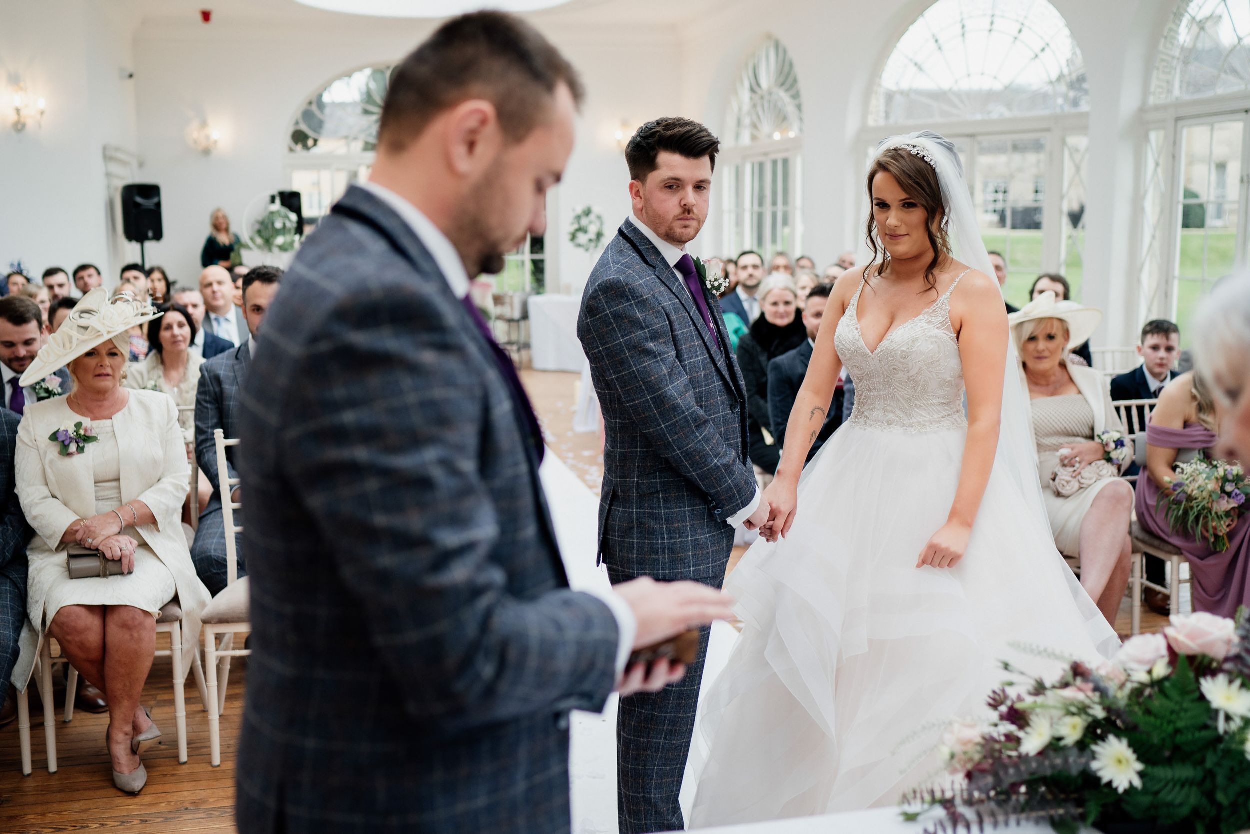 Elegant indoor wedding ceremony with white chairs and natural lighting.