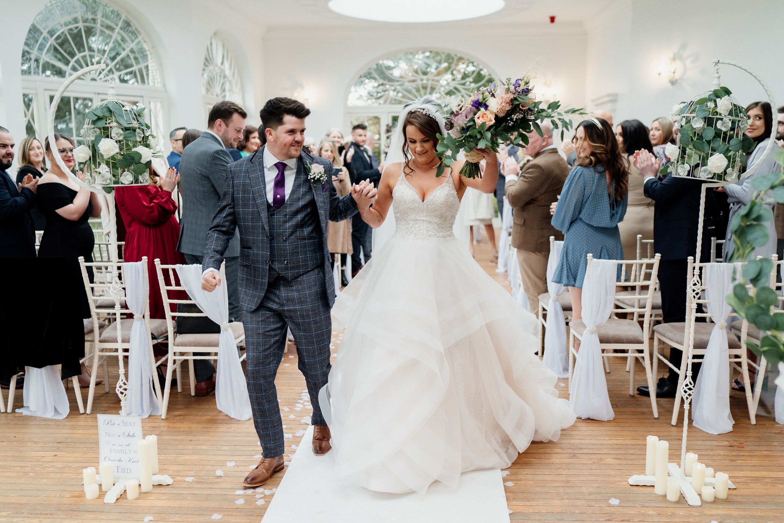 Wedding couple making their grand exit through an elegant white indoor venue.