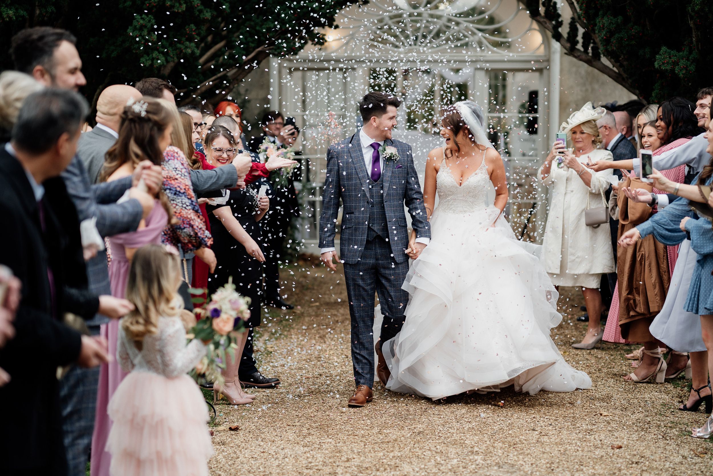 Guests shower the celebrating couple with confetti along a garden path outside Orangery at Barton Hall.
