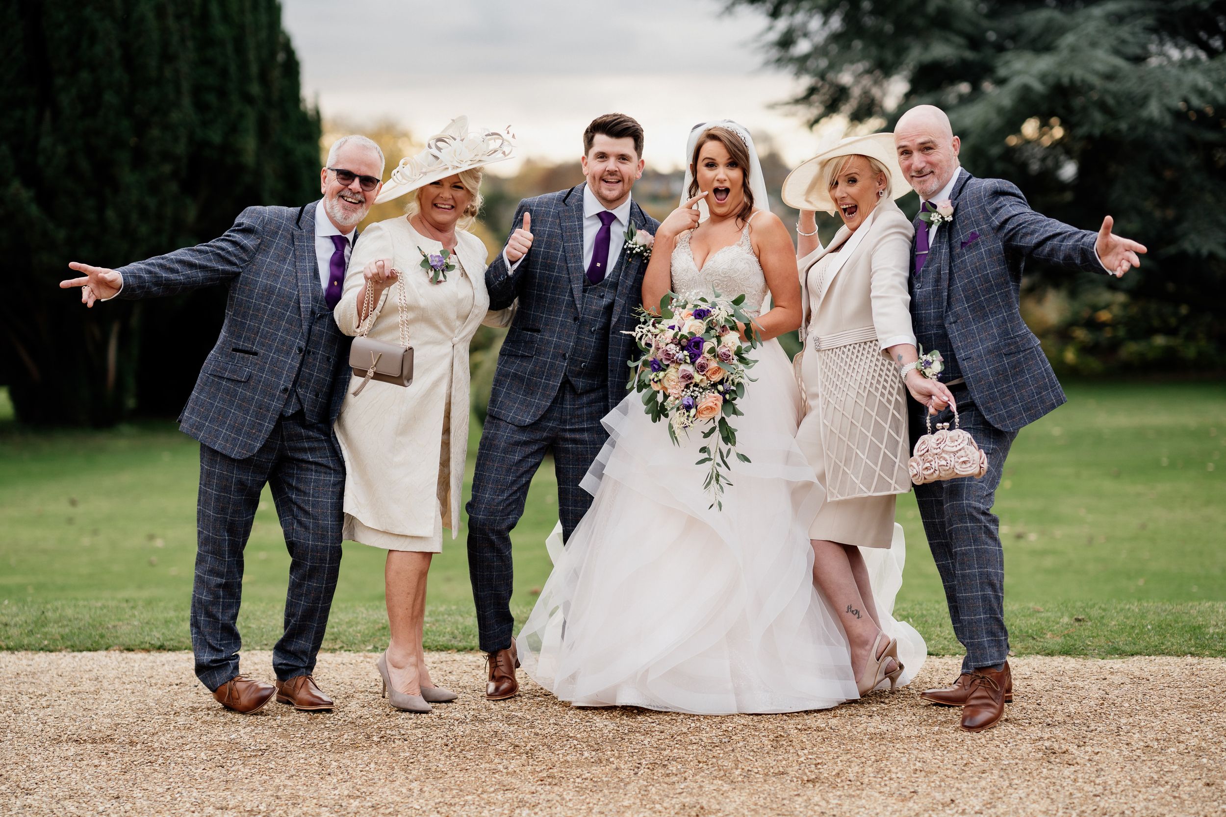 Wedding party poses playfully on garden path with bride in white gown center stage.