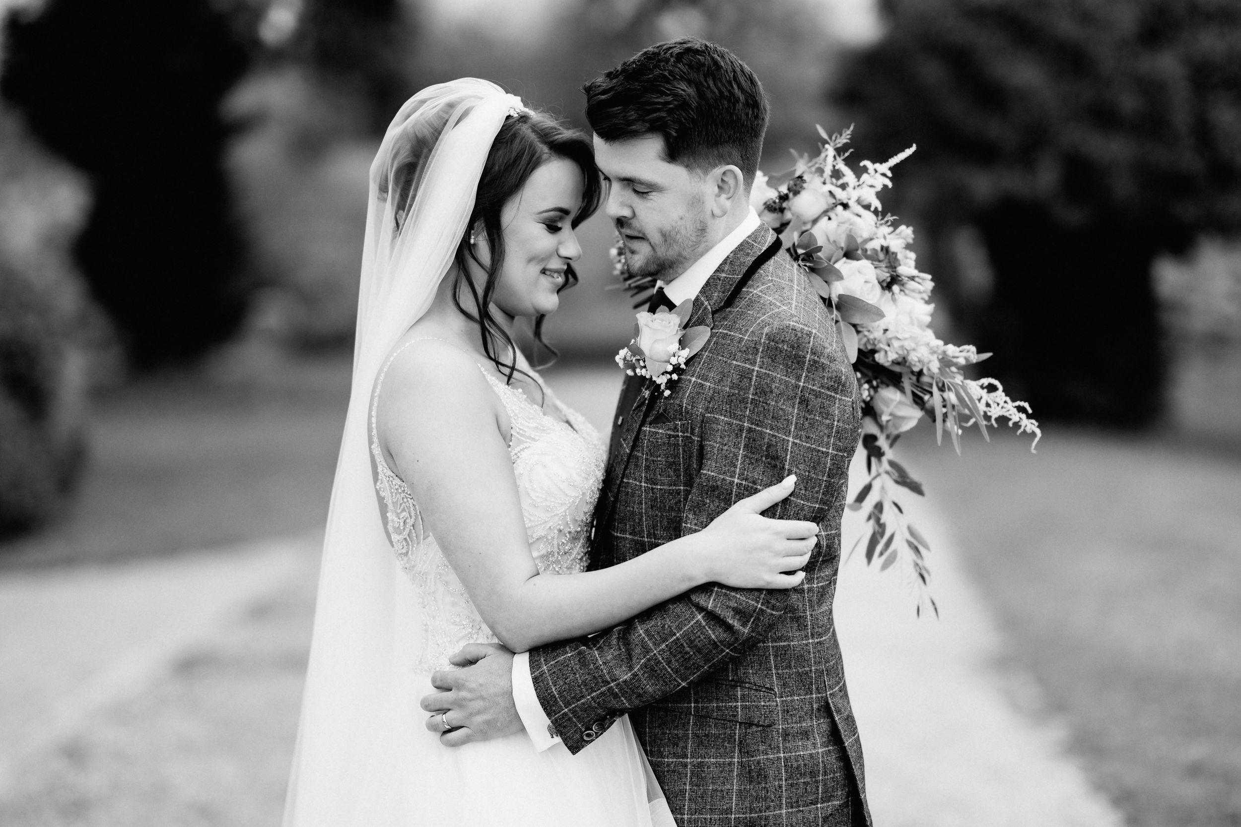 Black and white intimate portrait of couple in wedding attire with floral bouquet.