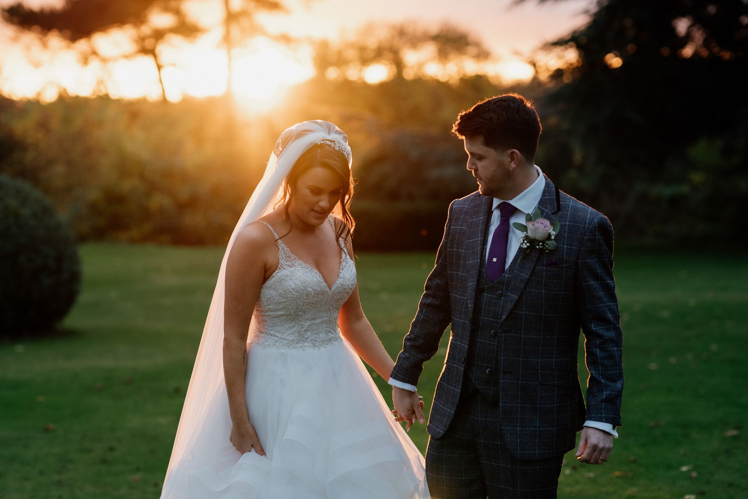 A couple shares an intimate moment during their sunset wedding photoshoot on manicured grounds.