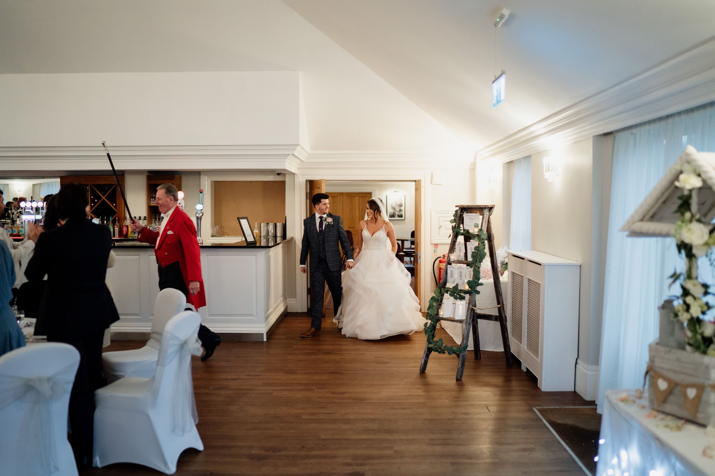 Wedding guests mingle in an elegant indoor reception venue with wooden floors and white decor.