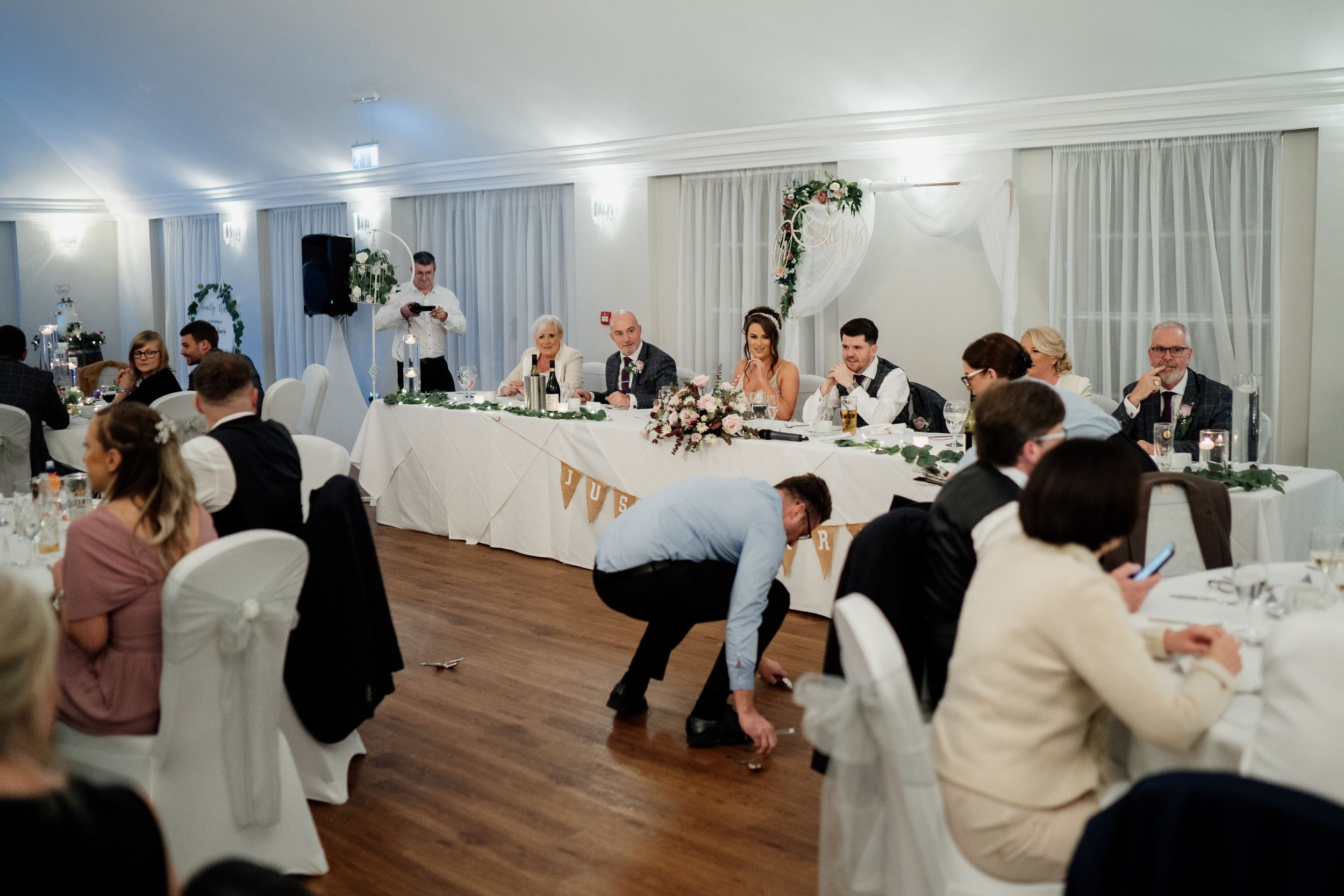 Wedding reception at Barton Hall guests seated at decorated tables in an elegant white room with hardwood floors.