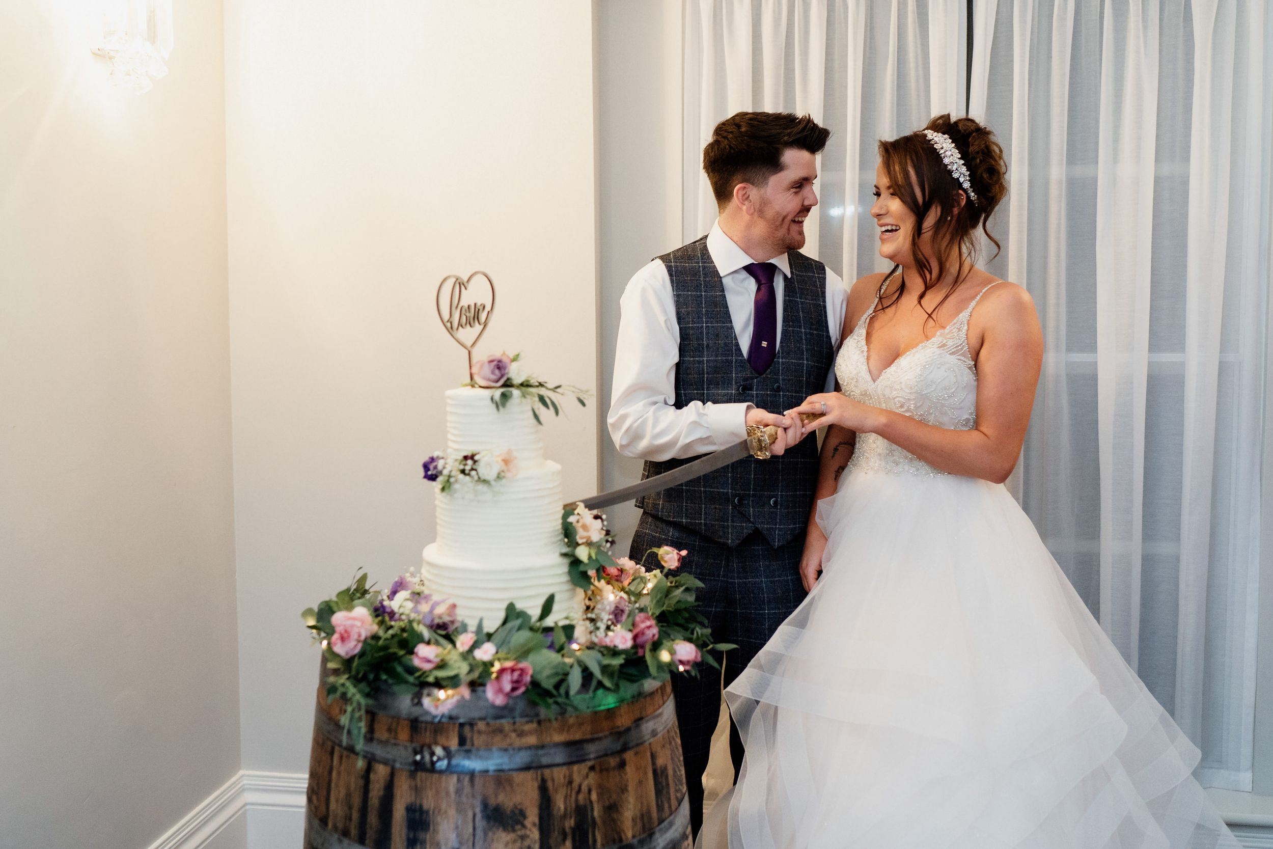 Newlyweds share a moment beside a rustic wine barrel decorated with floral arrangements.