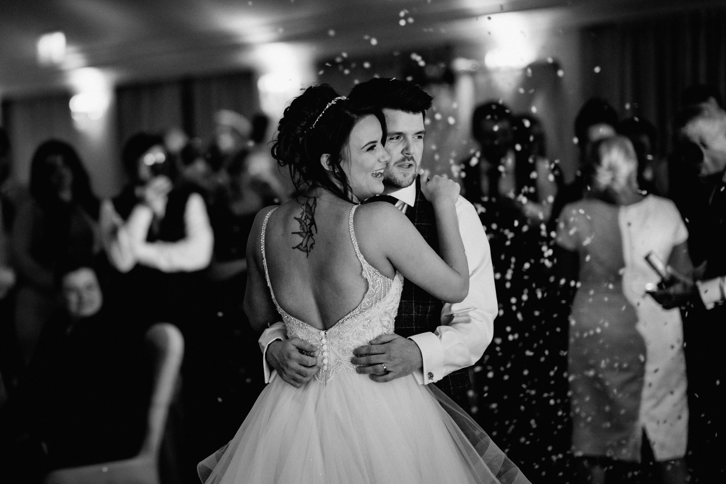 A black and white photo of a couple sharing their first dance at a wedding reception with sparkles in the background.