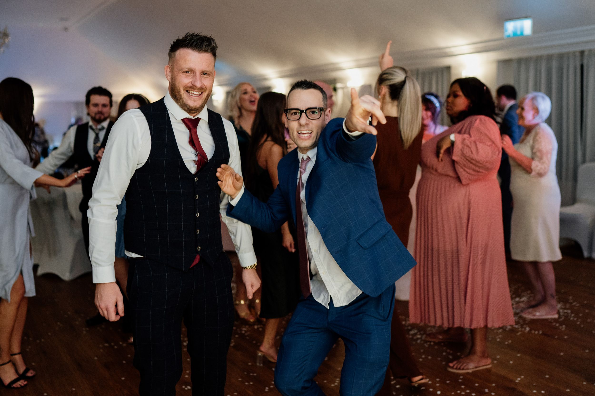 Guests enjoying themselves on the dance floor at a wedding reception in formal attire.