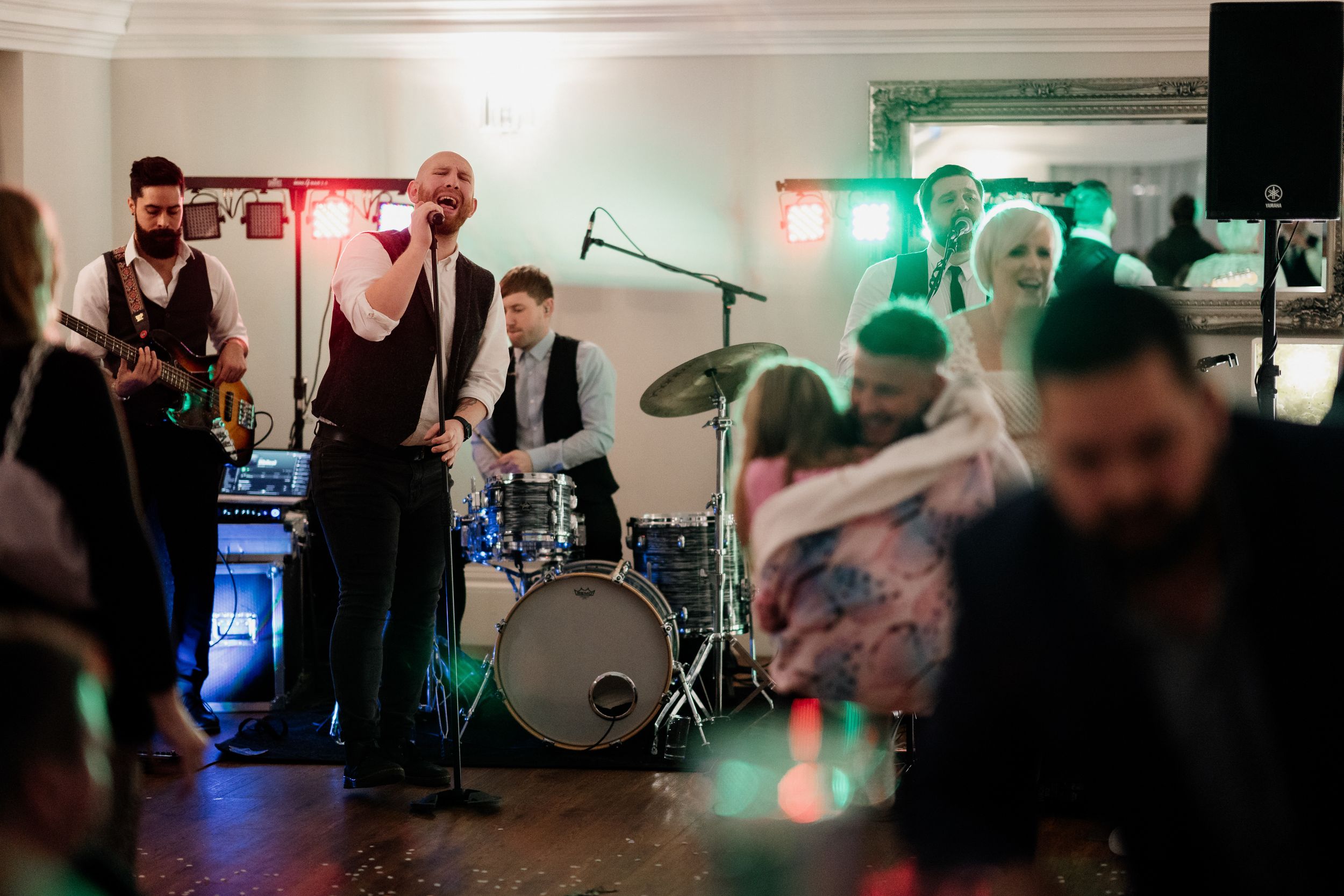 Live band performing at wedding reception with drum kit and colored lighting visible.