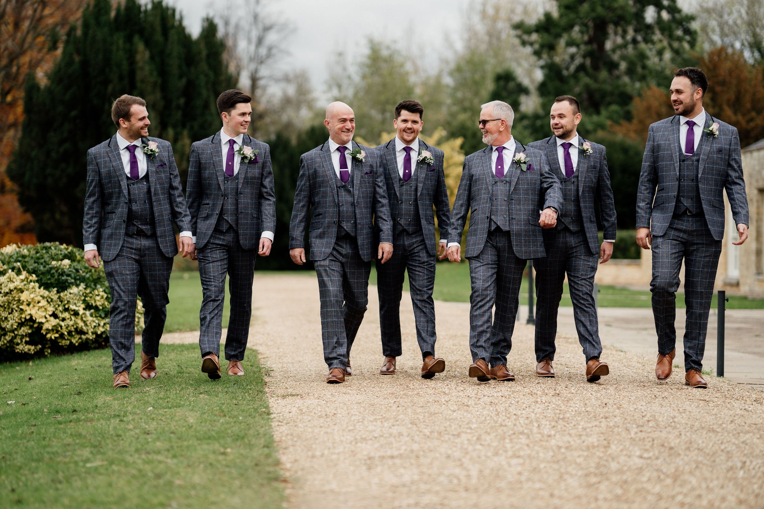 Wedding party in matching gray suits walking together on garden pathway.