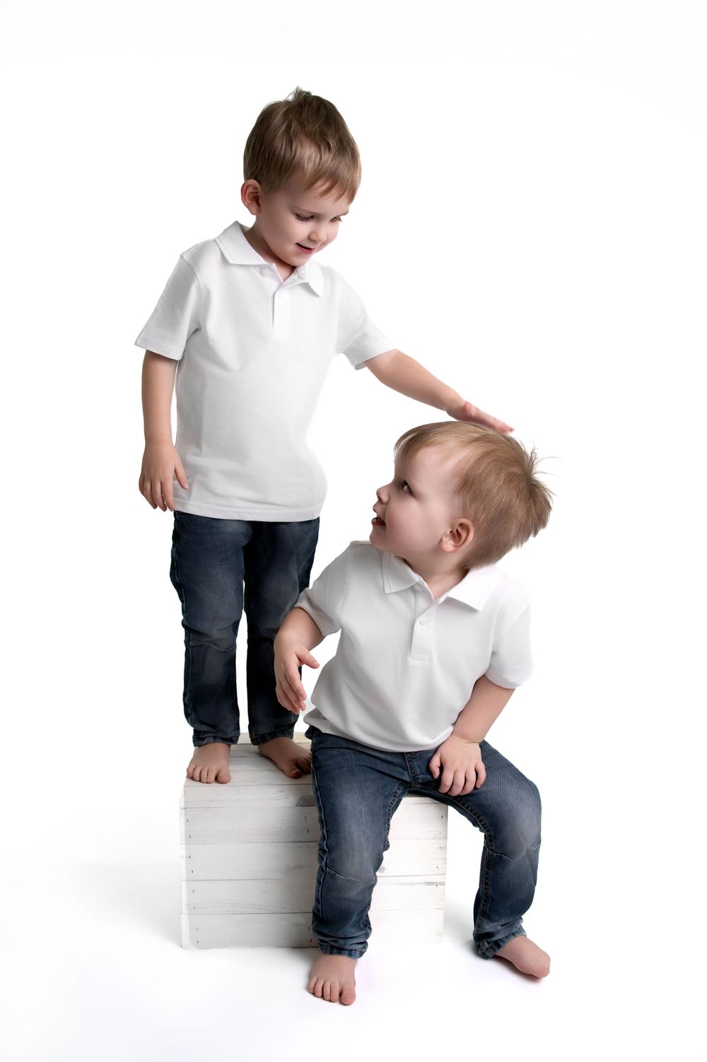 Two children in matching white polo shirts and jeans posing playfully against white background.