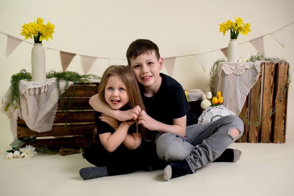 Children pose together on floor for professional photo with rustic wooden crates and yellow daffodil decorations.