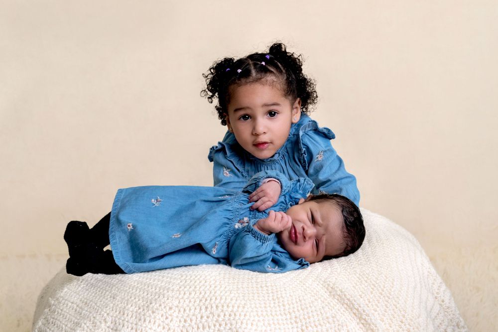 Two siblings in matching powder blue outfits share a playful moment while posing on a white textured backdrop.