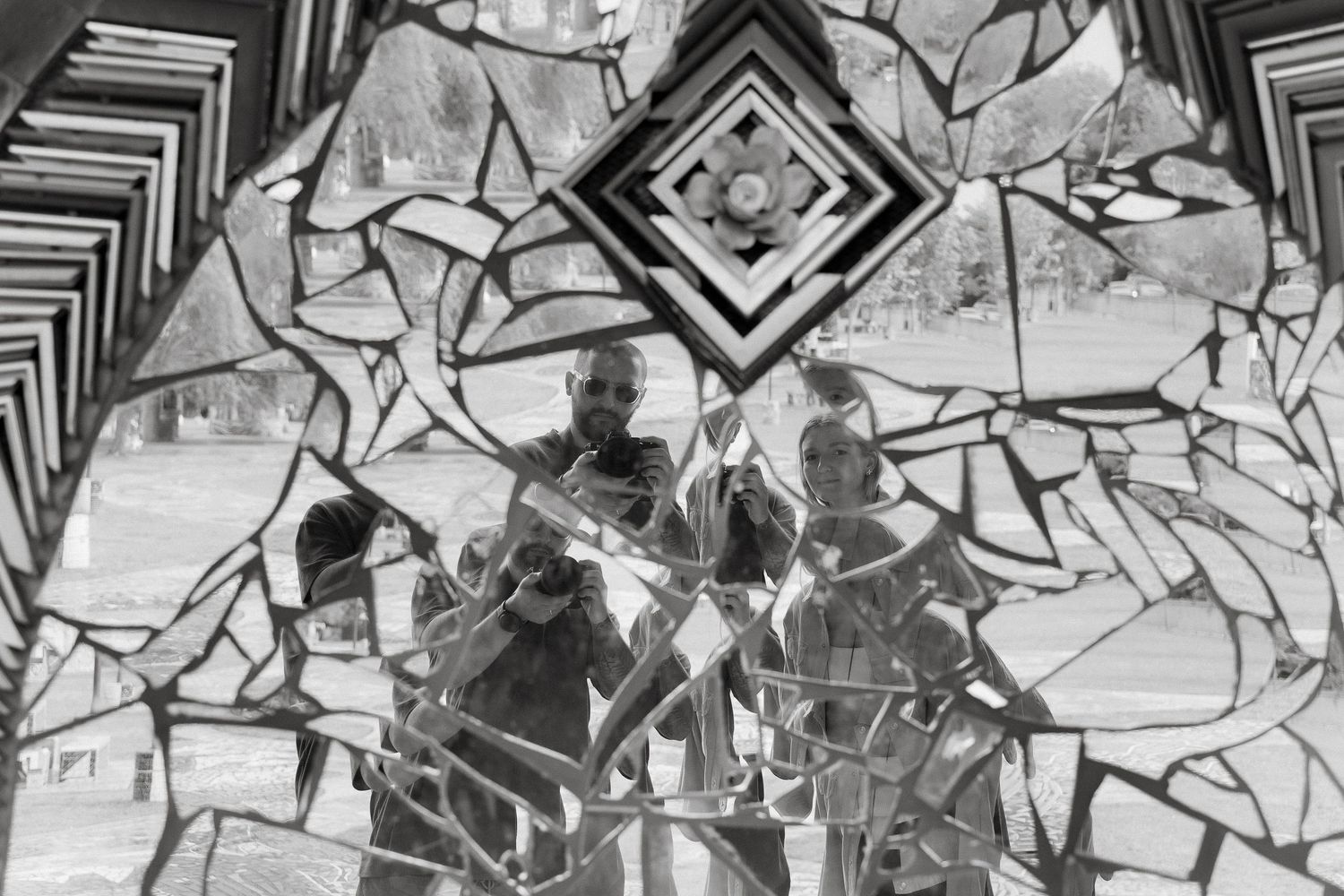 Black and white abstract photograph showing silhouettes through a geometric kaleidoscope-like pattern of broken glass.