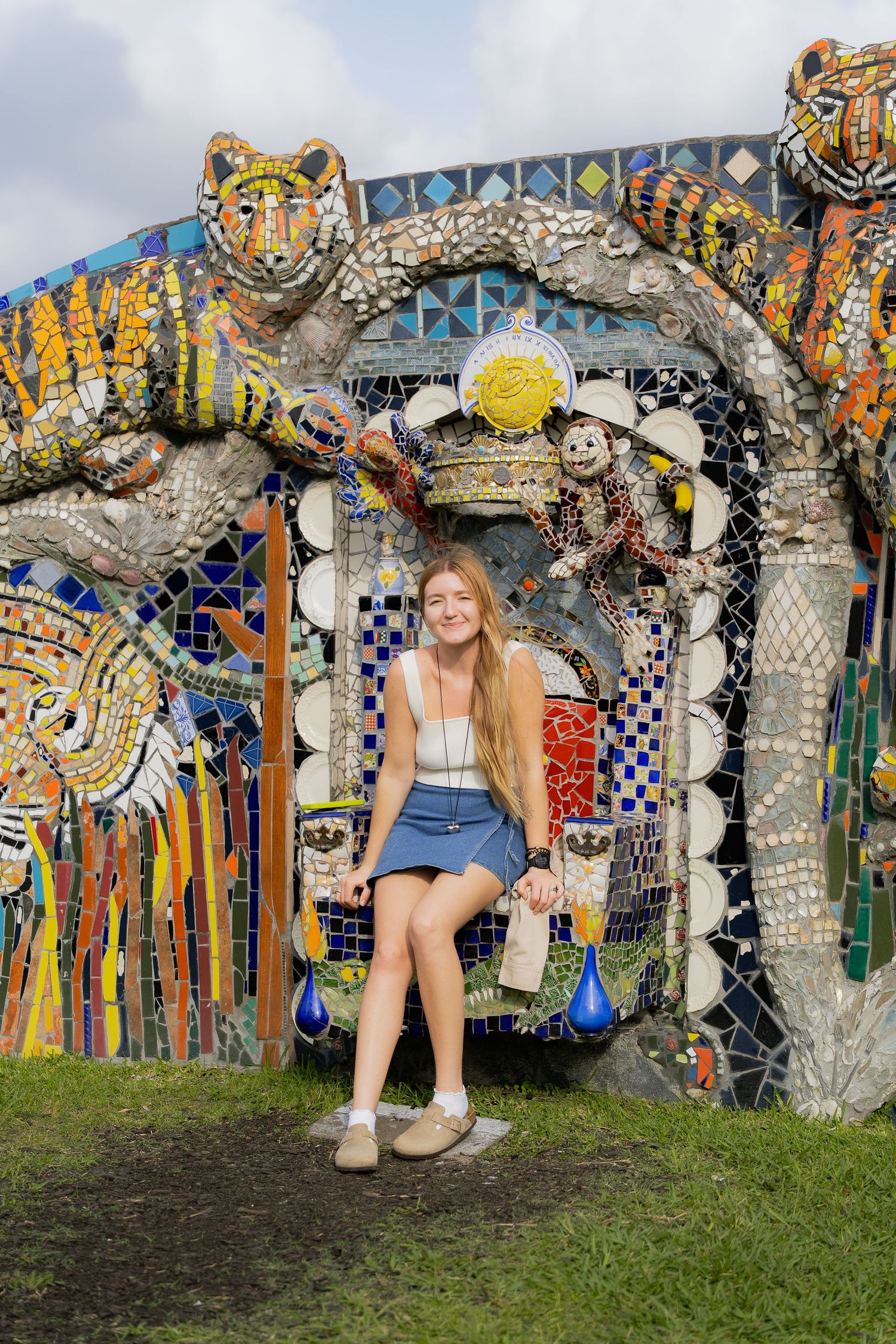 Colorful mosaic art installation featuring tiger designs and decorative archway in an outdoor garden setting.