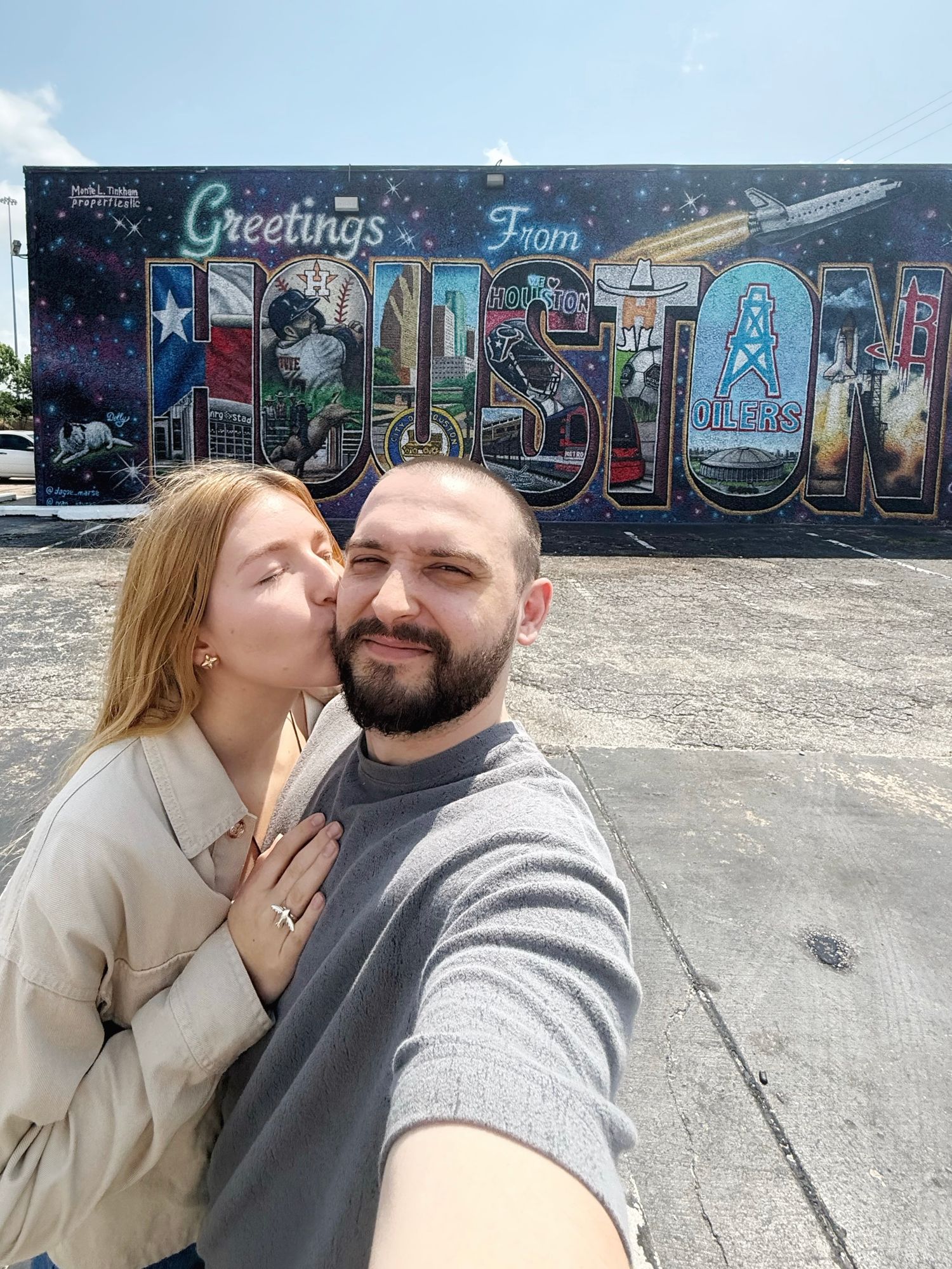 A couple takes a selfie in front of a colorful Houston graffiti mural wall with blue sky in the background.
