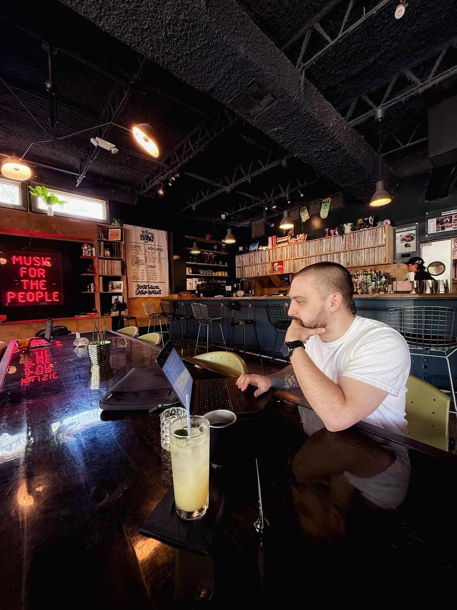 Someone enjoys a cold cocktail at a dimly lit bar with neon signs and industrial decor.